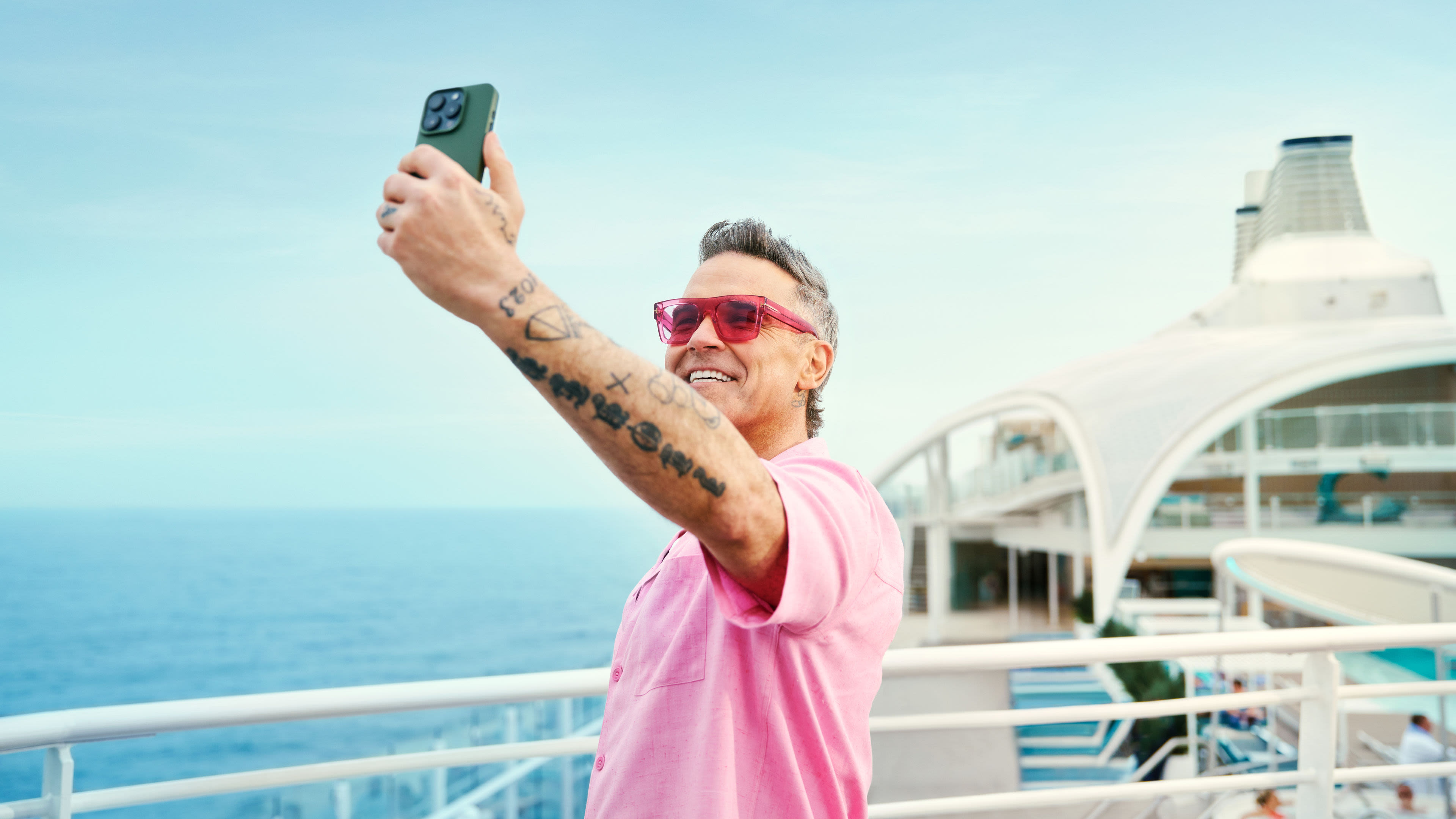 Mein-Schiff rocks - Robbie Williams Mann in rosa Hemd macht Selfie auf Kreuzfahrtschiff.