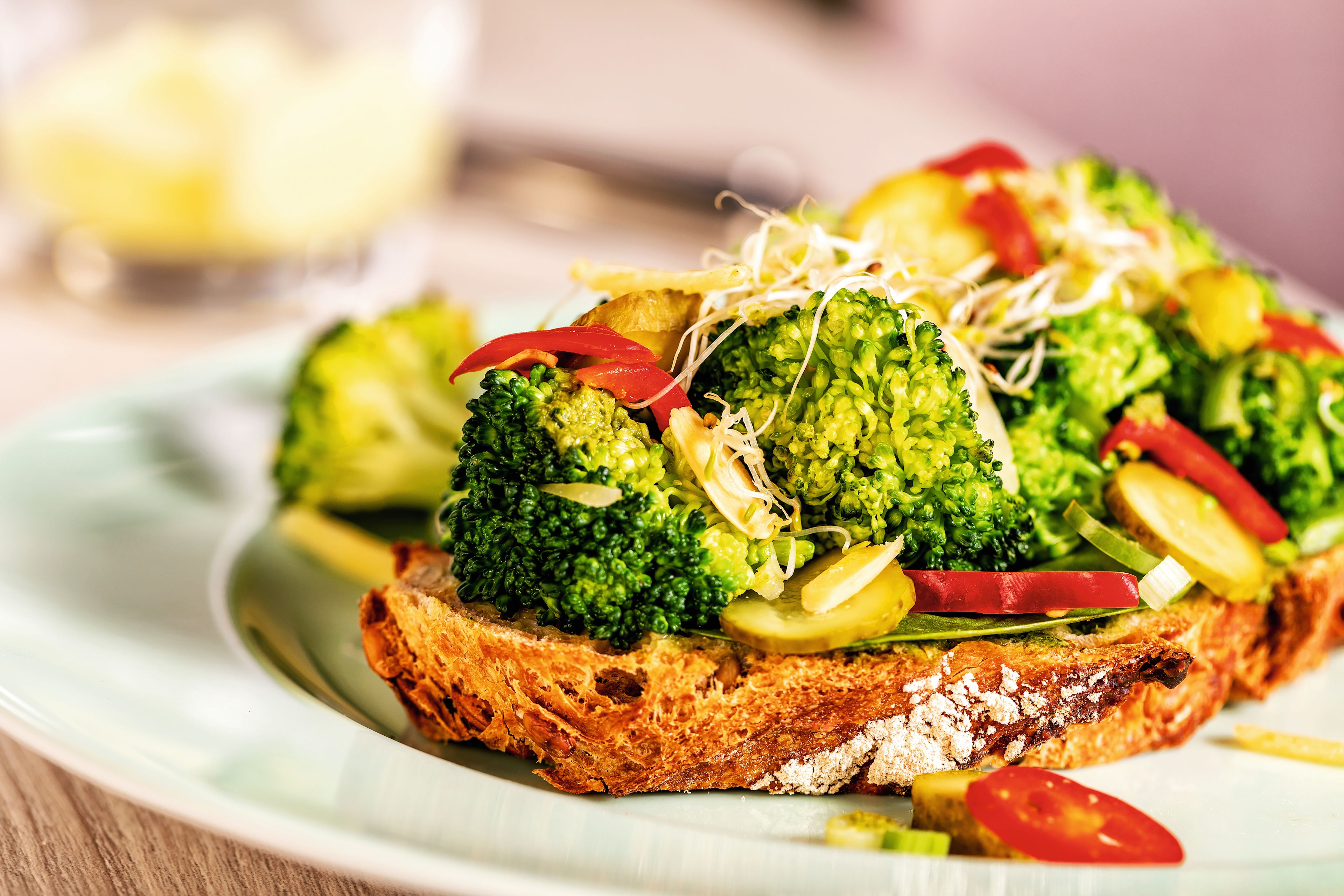 Brot mit Brokkoli, Paprika und Sprossen auf Teller.
