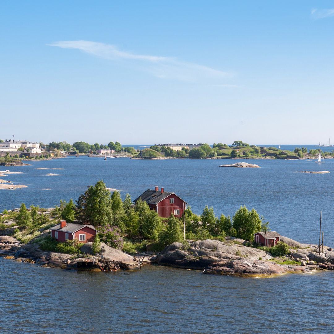 Rote Häuser auf kleiner Insel im finnischen Archipel, blauer Himmel.
