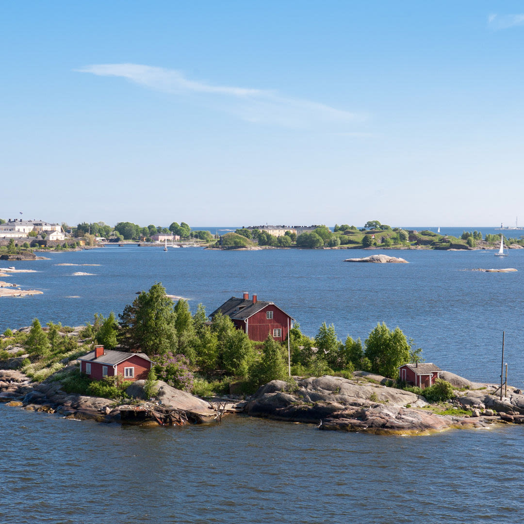 Rote Häuser auf kleiner Insel im finnischen Archipel, blauer Himmel.