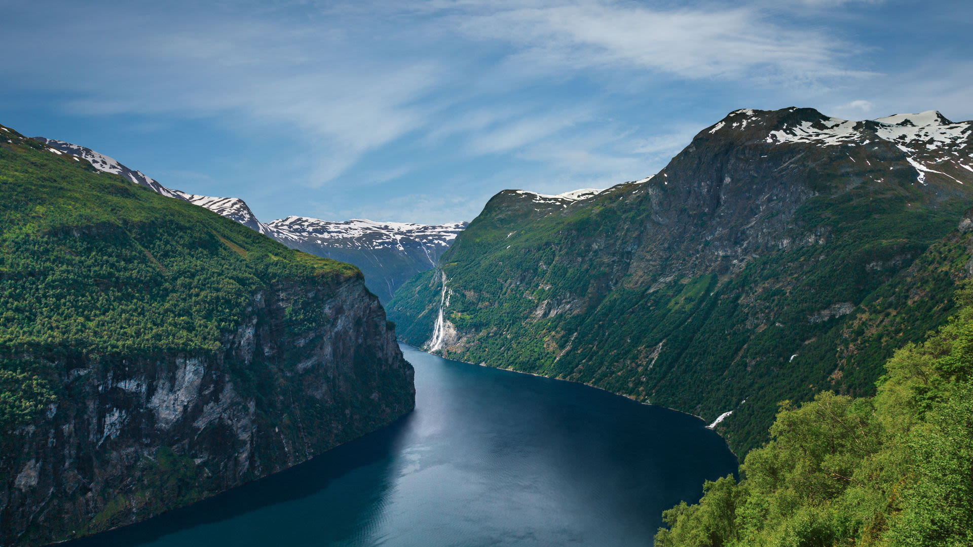 Norwegischer Fjord mit Wasserfall, umgeben von grünen Bergen und blauem Himmel. Norwegischer Fjord mit Wasserfall, umgeben von grünen Bergen und blauem Himmel.