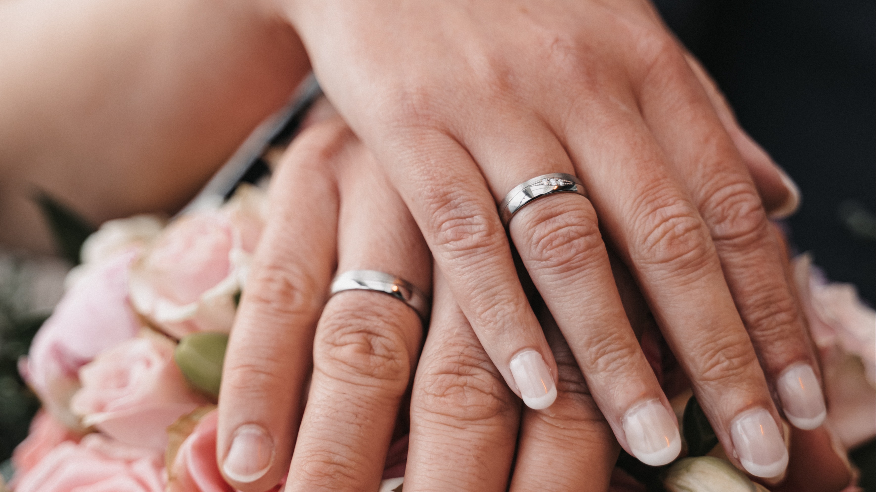 Hände mit Eheringen auf rosa Rosenstrauß.