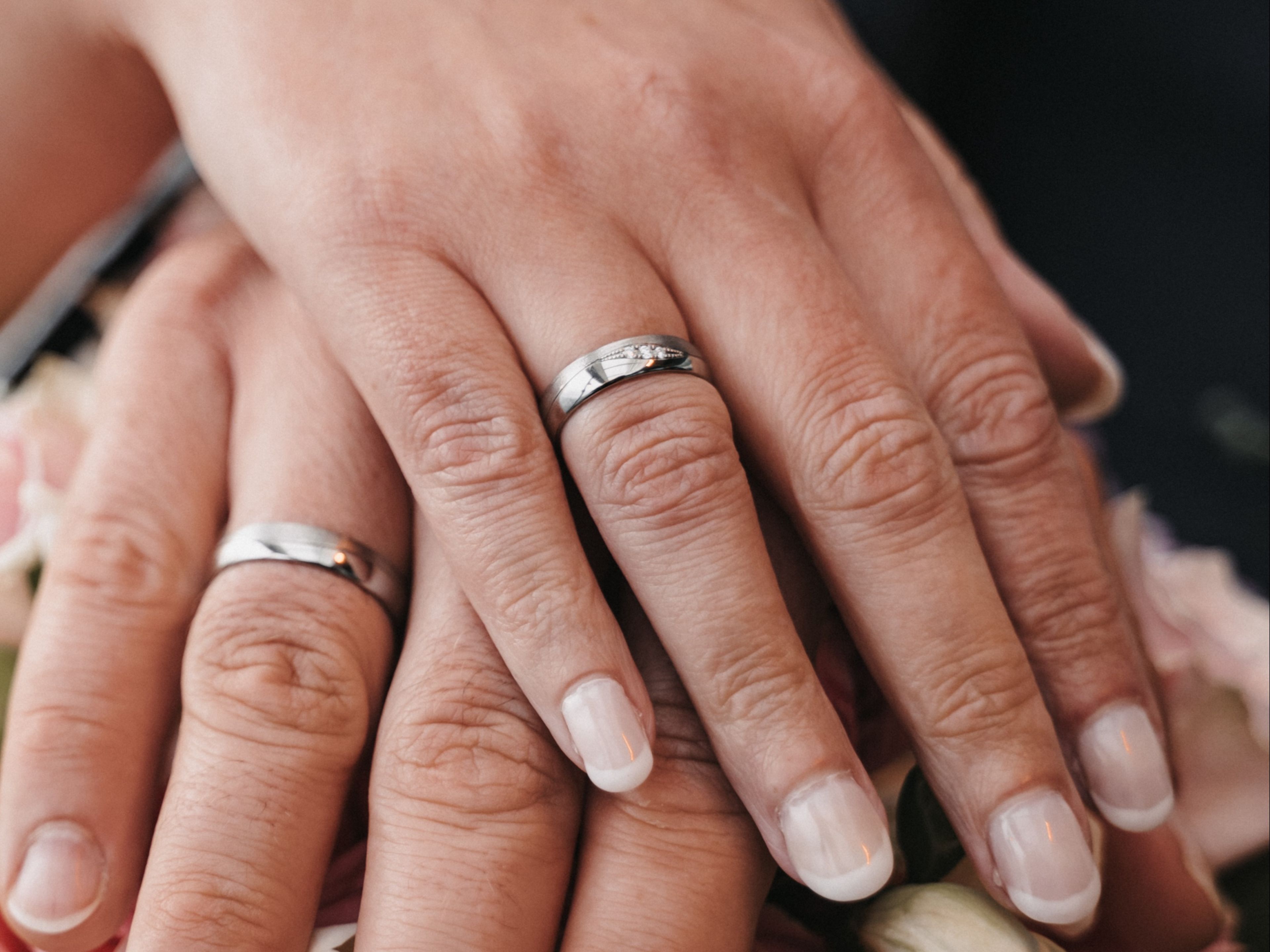 Kirchliche Trauung (4) Hände mit Eheringen auf rosa Rosenstrauß.