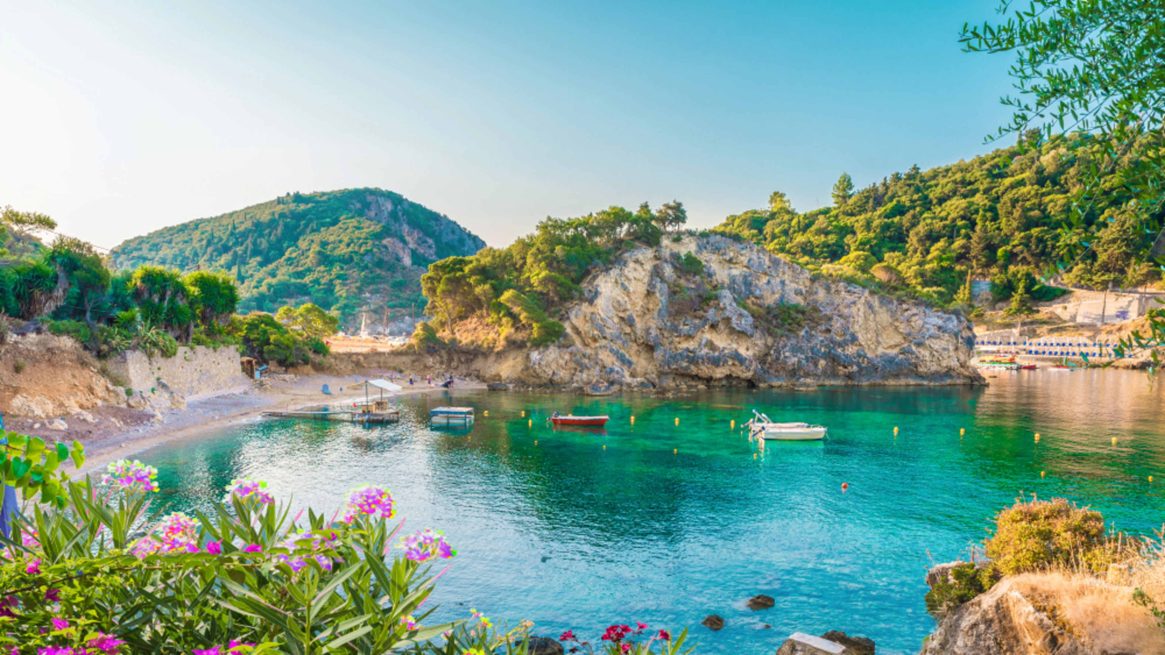 Griechenland Bucht auf Korfu mit türkisfarbenem Wasser, Booten und Blumen.