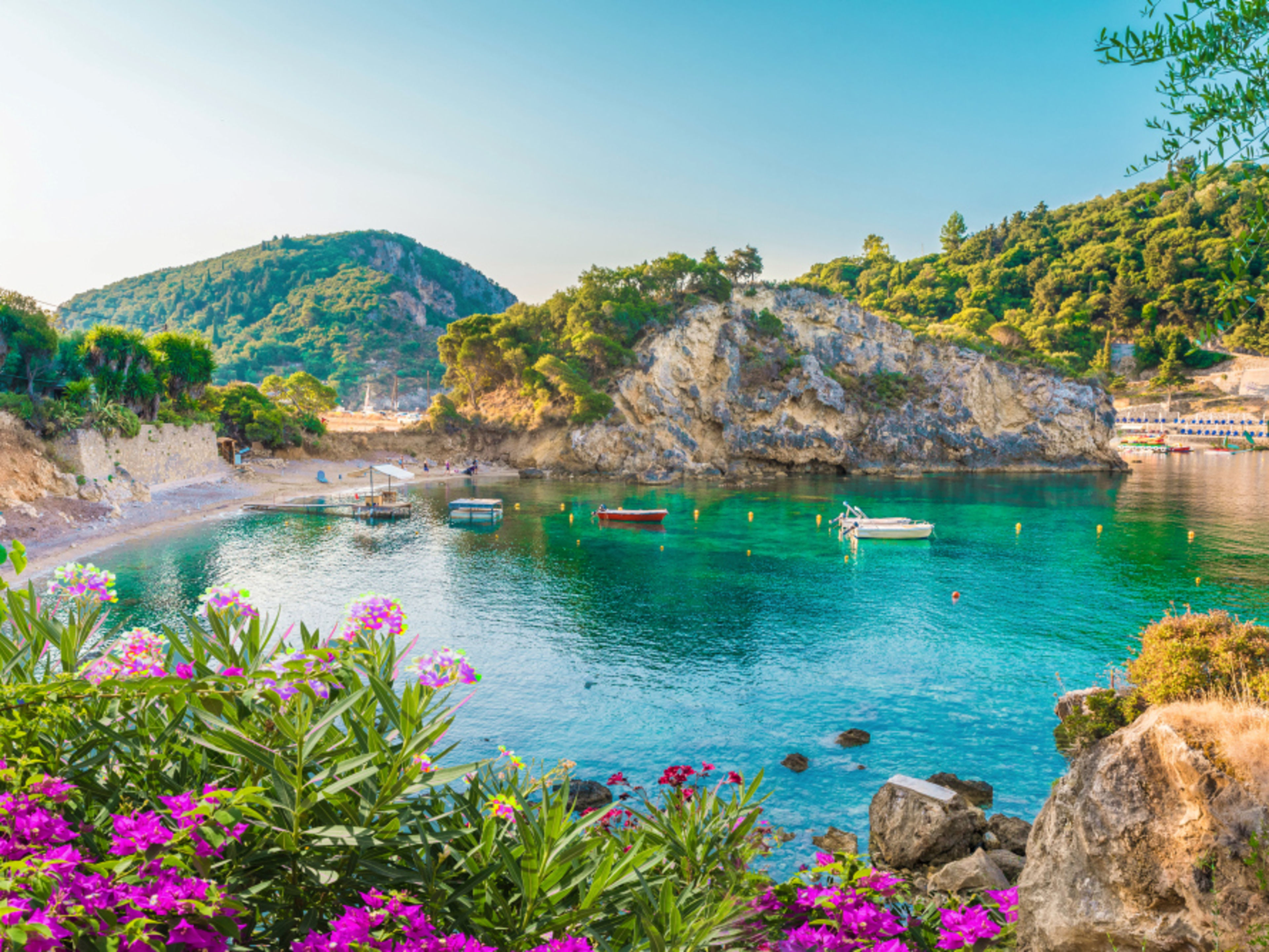 Griechenland Bucht auf Korfu mit türkisfarbenem Wasser, Booten und Blumen.