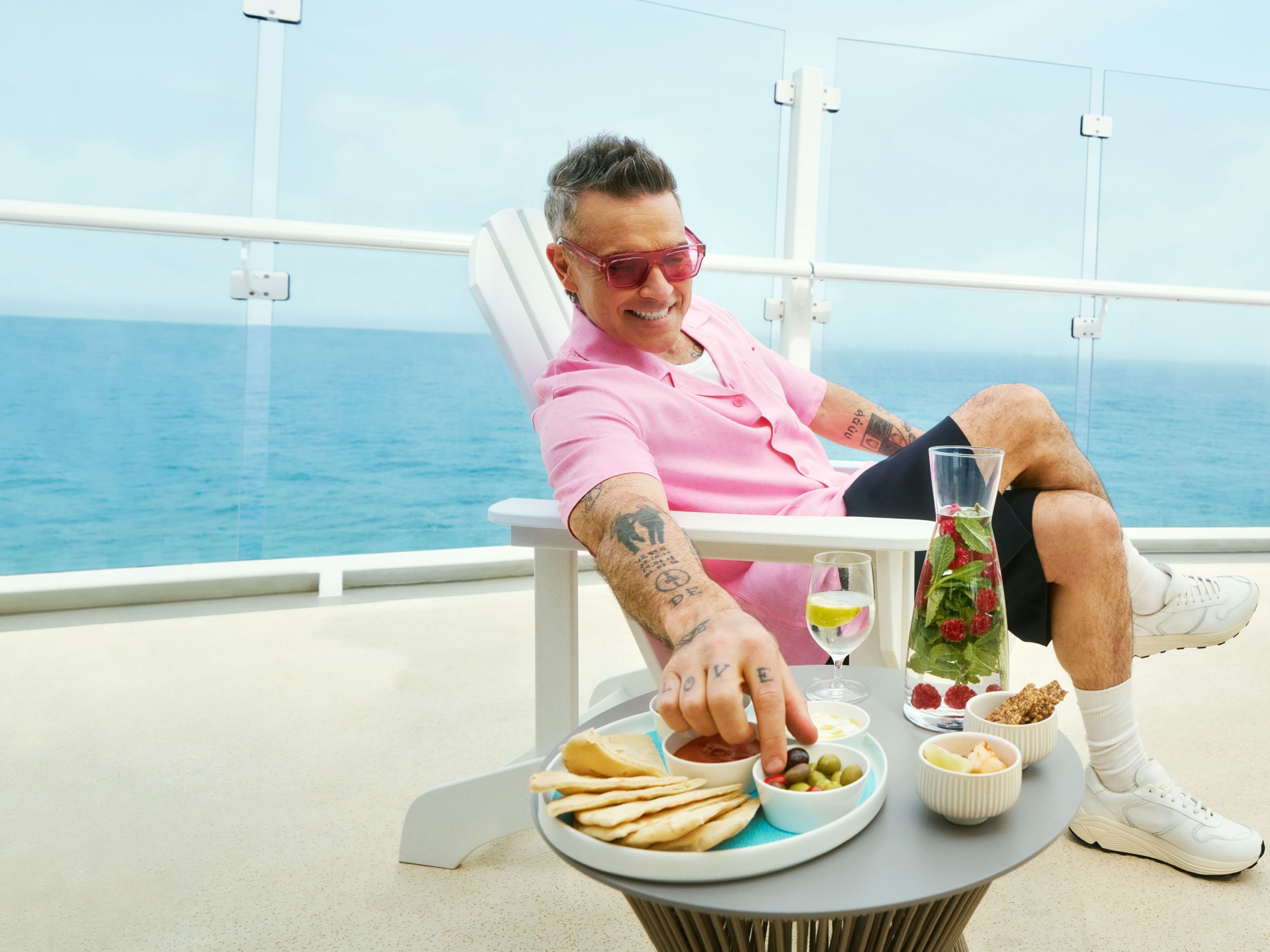 Robbie Williams - Mein-Schiff rocks Mann in rosa Hemd entspannt auf Kreuzfahrtschiff, Snacks und Getränke.