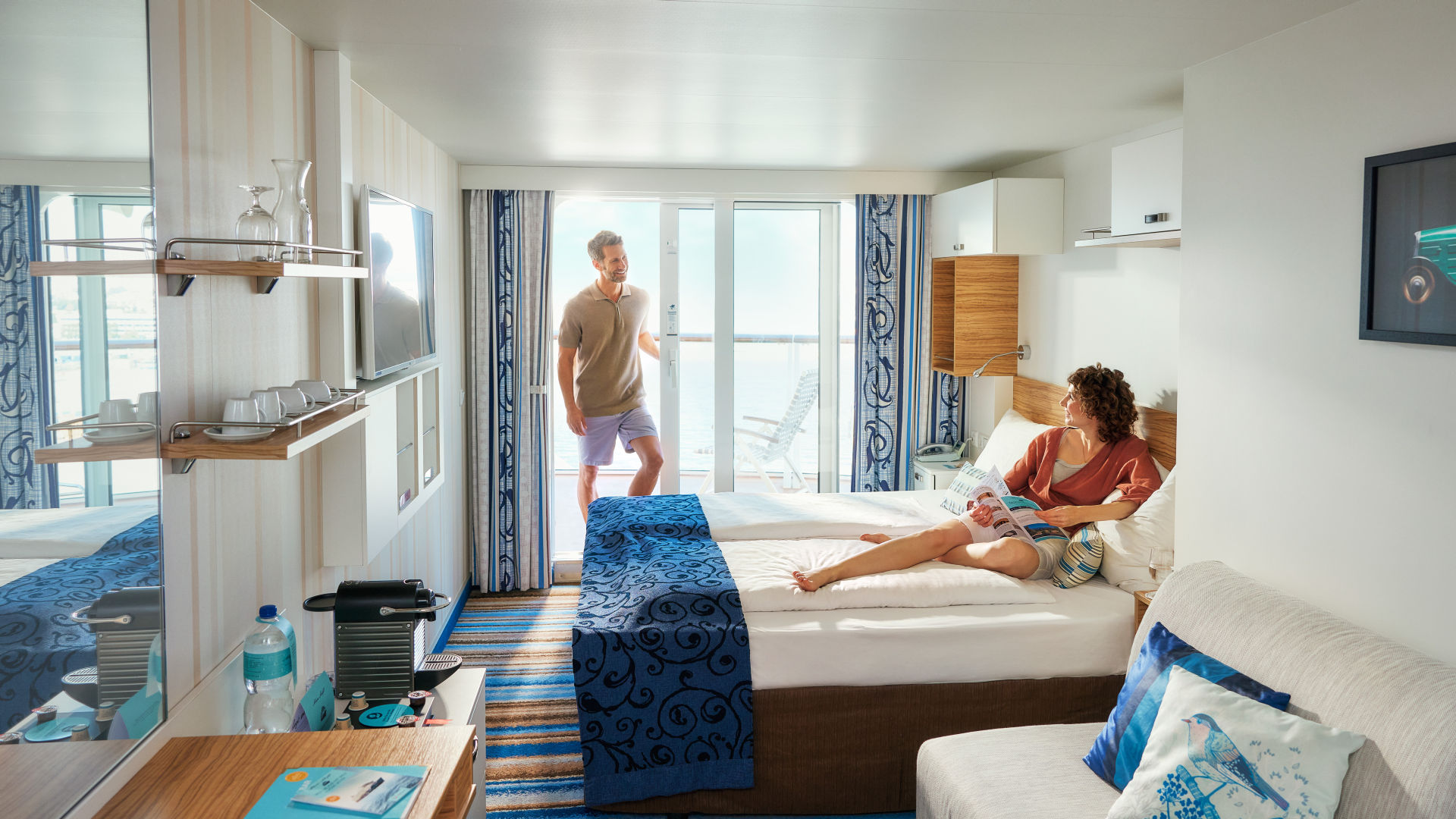 Paar entspannt in moderner Kreuzfahrtkabine mit Balkon und Meerblick.