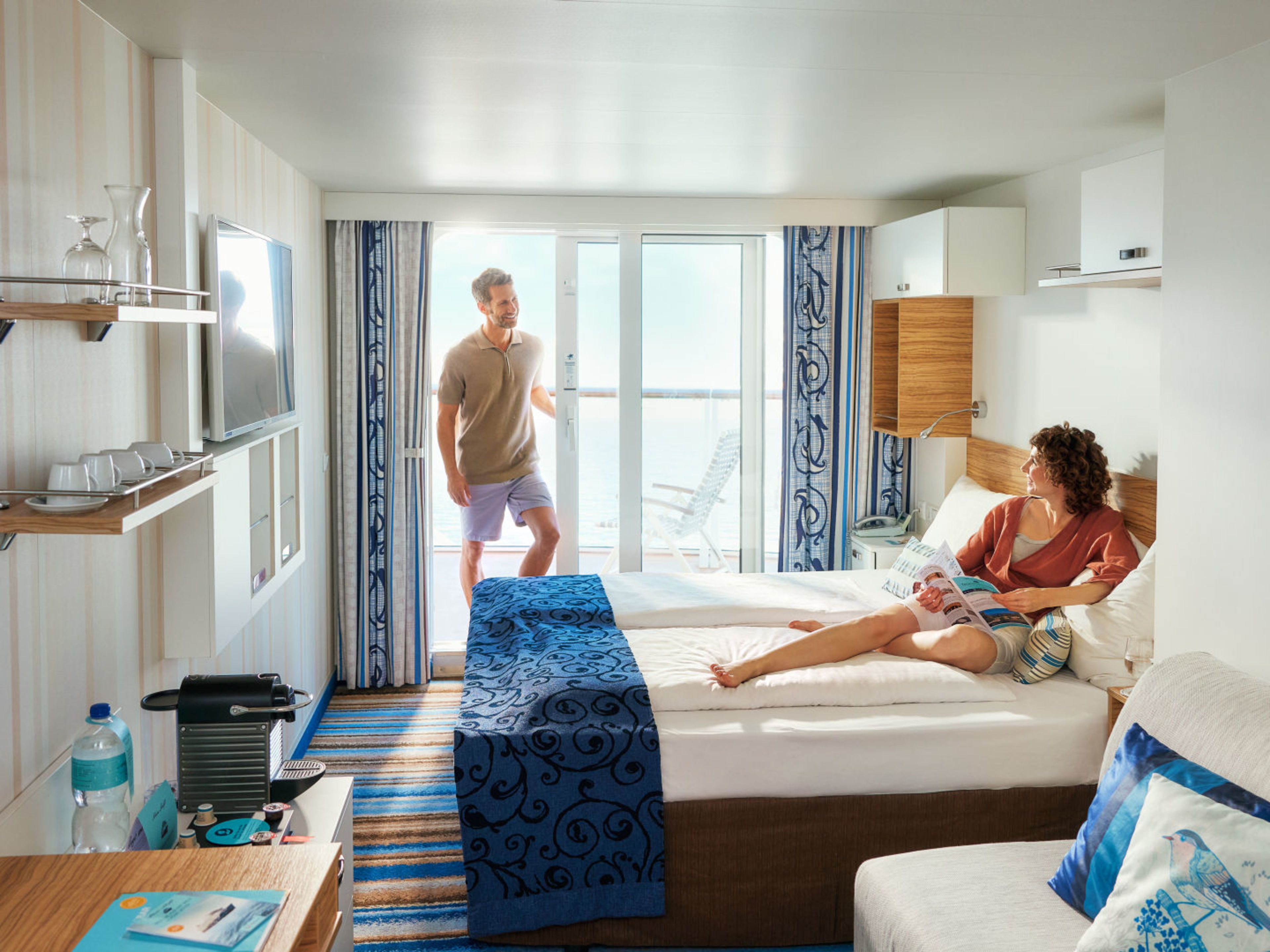 Paar entspannt in moderner Kreuzfahrtkabine mit Balkon und Meerblick. Paar entspannt in moderner Kreuzfahrtkabine mit Balkon und Meerblick.