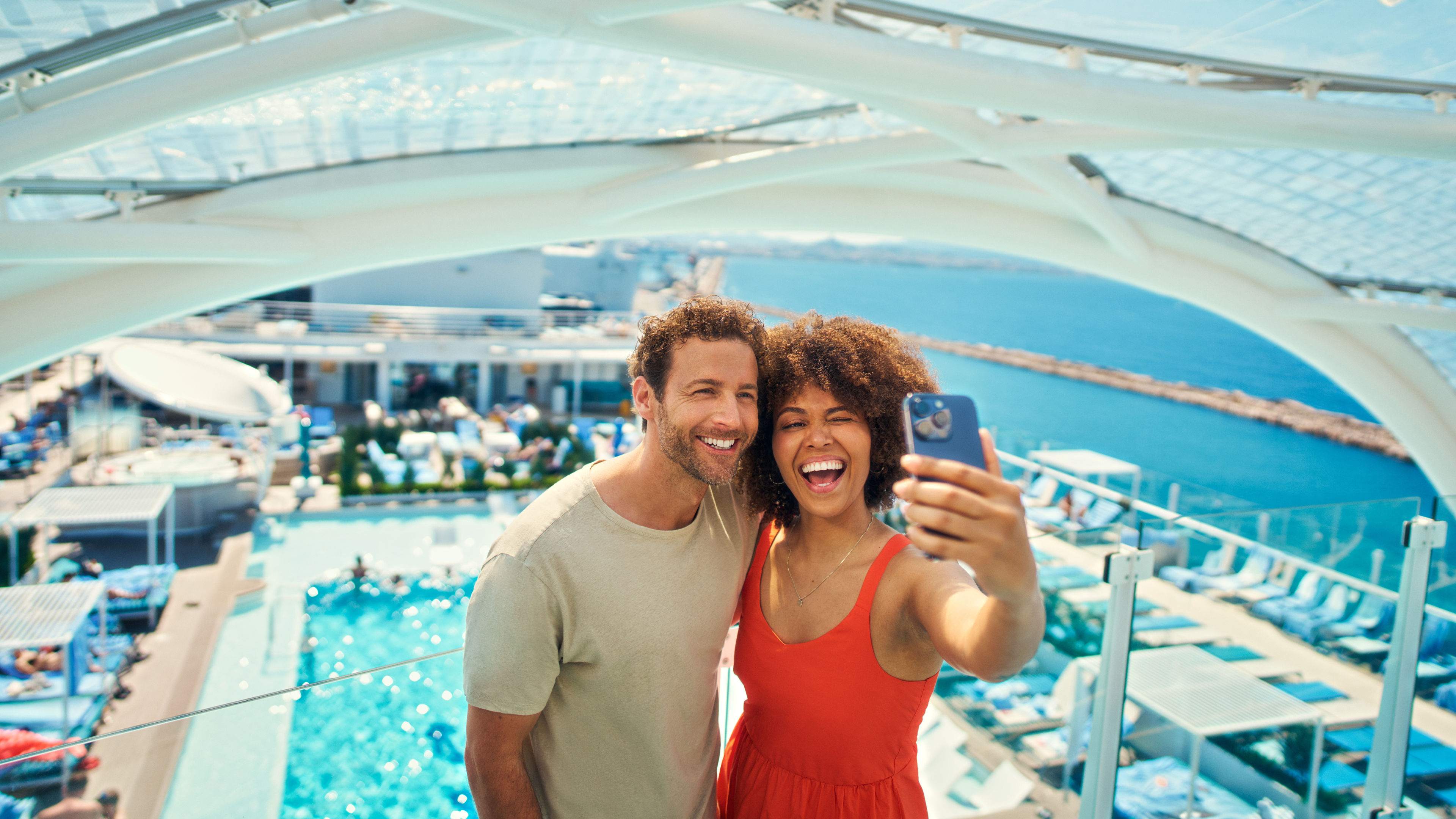 Paar macht Selfie auf Kreuzfahrtschiff der Mein Schiff® Flotte, Pool im Hintergrund.