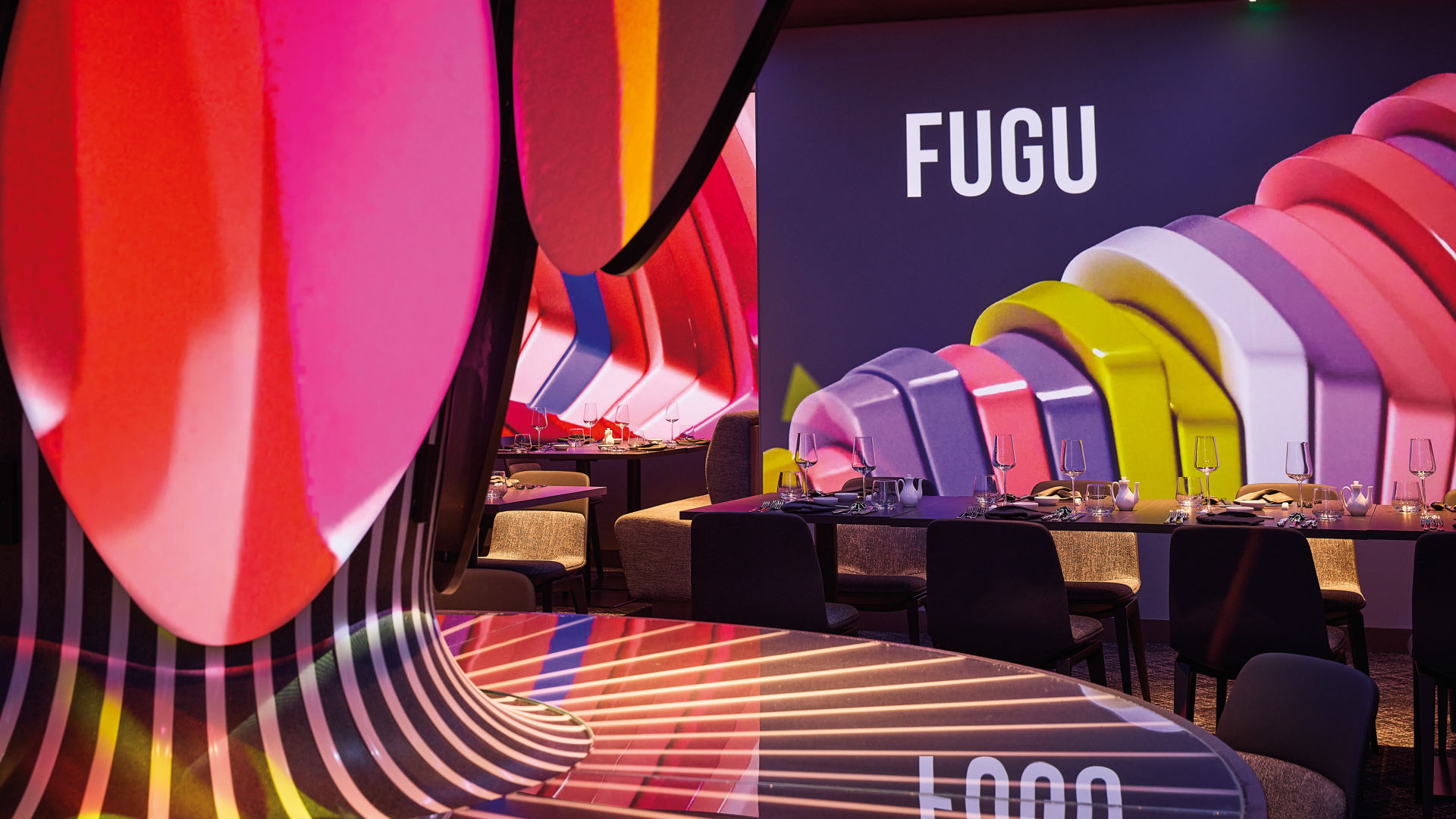 Buntes Restaurantinterieur mit Tischen, Stühlen und FUGU-Schriftzug.