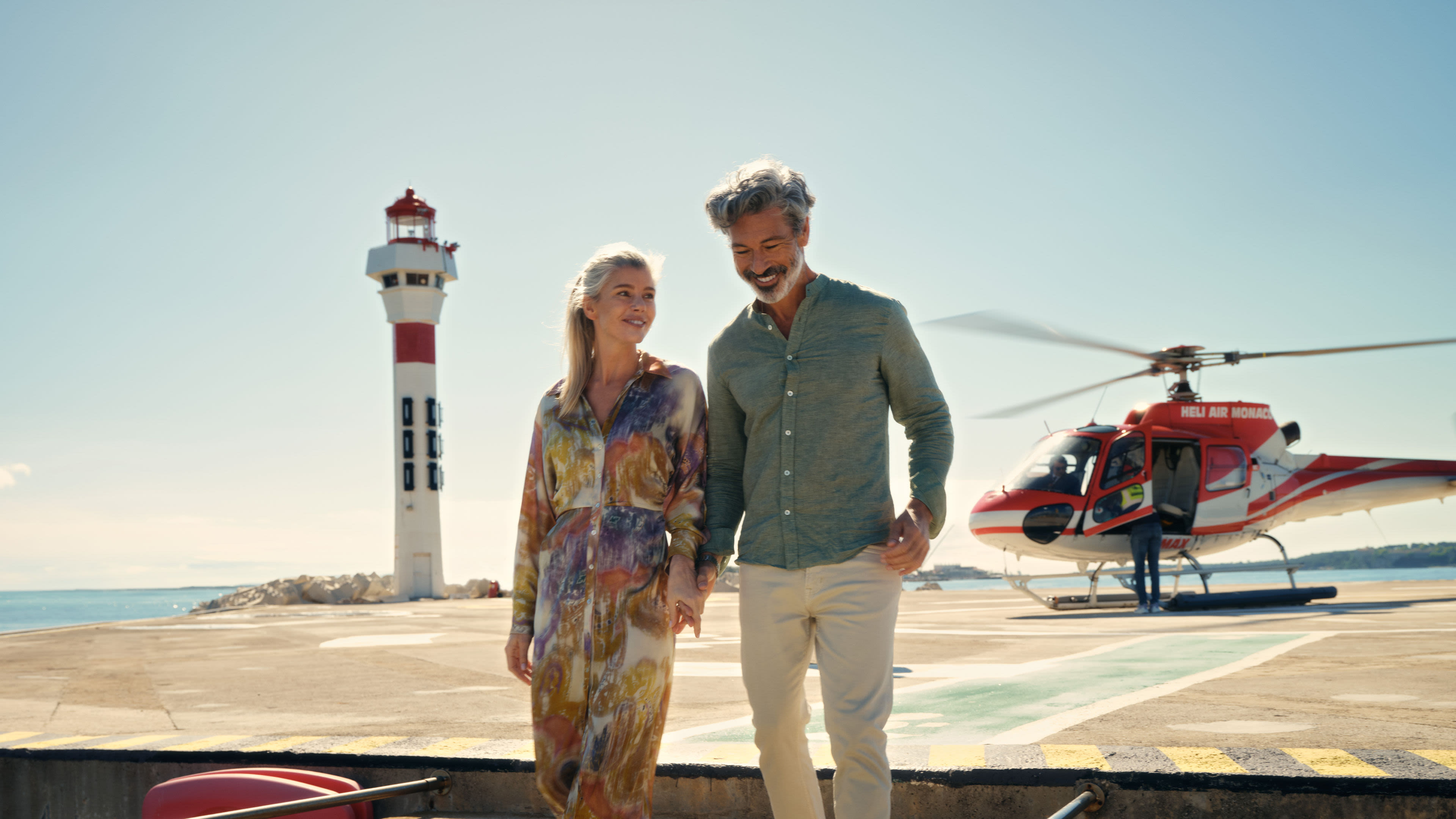 Landausflüge Concierge Service Paar spaziert am Leuchtturm, roter Hubschrauber im Hintergrund.