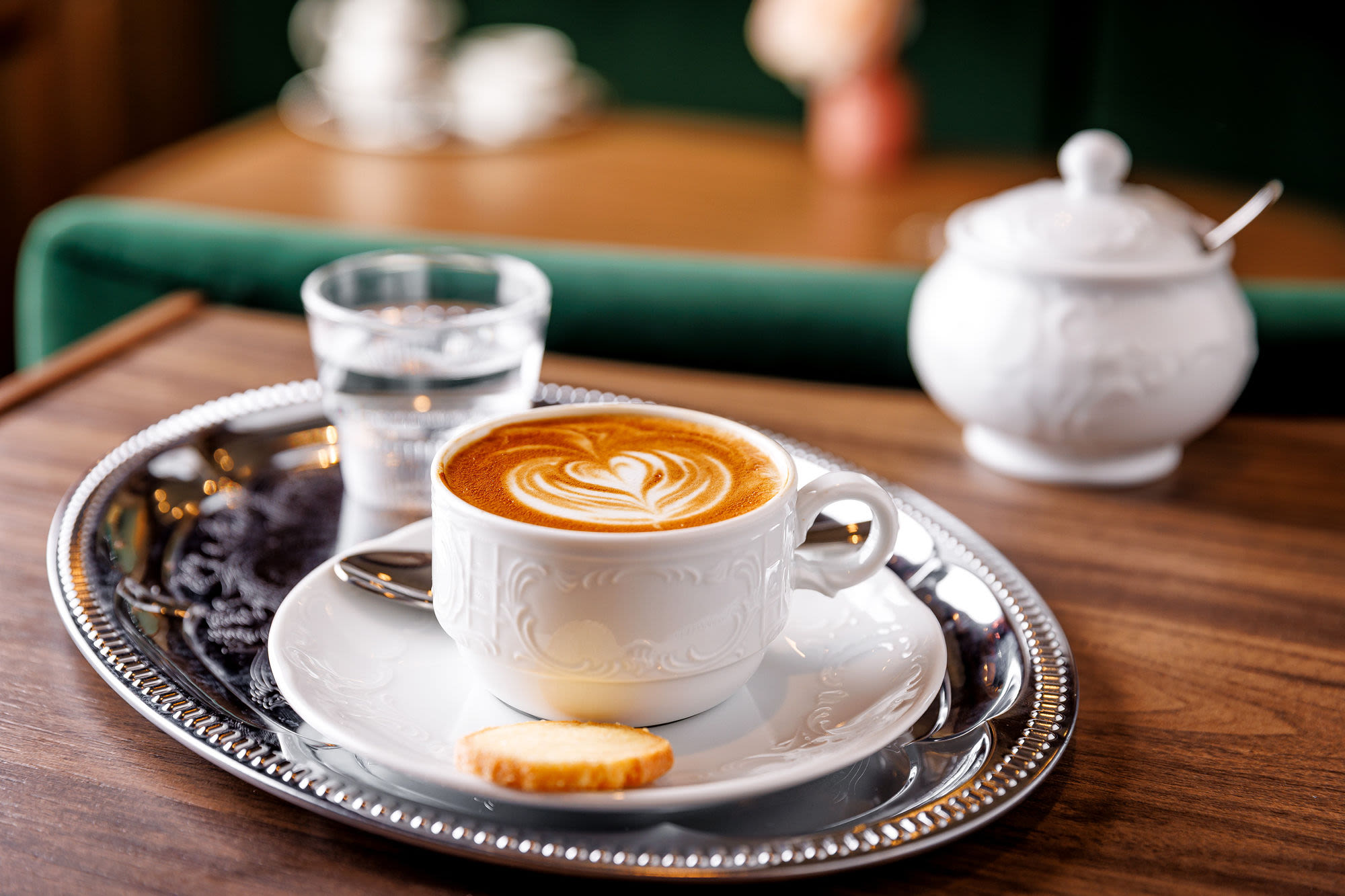 Kaffee mit Latte Art auf Tablett, Keks, Glas Wasser. Kaffee mit Latte Art auf Tablett, Keks, Glas Wasser.