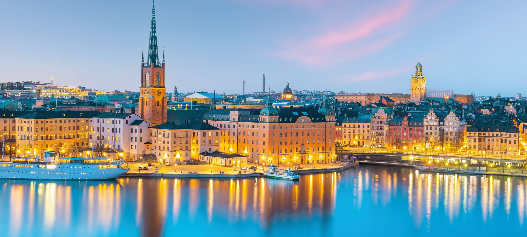 Stockholm bei Dämmerung, beleuchtete Gebäude und Kirche am Wasser.