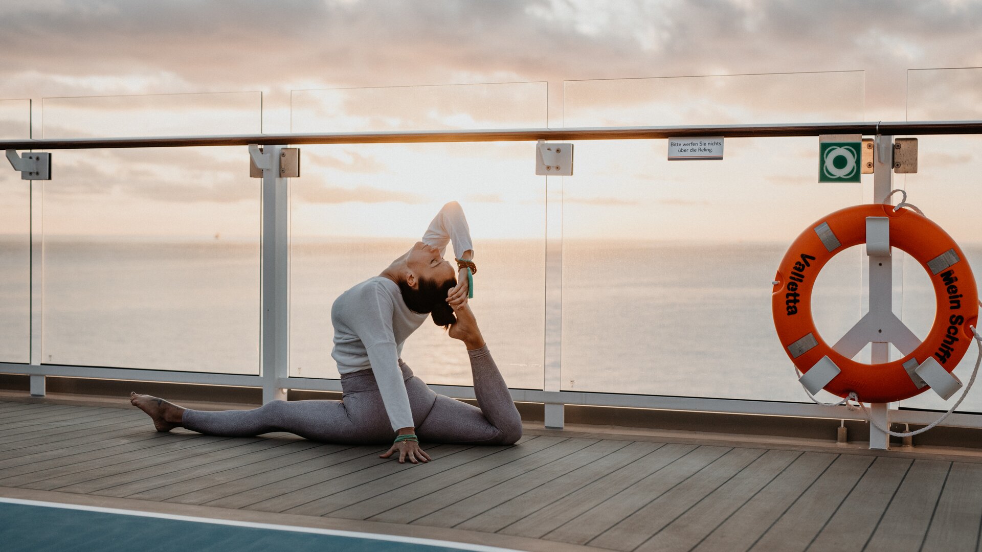Frau macht Yoga auf Kreuzfahrtschiff der Mein Schiff® Flotte bei Sonnenuntergang.