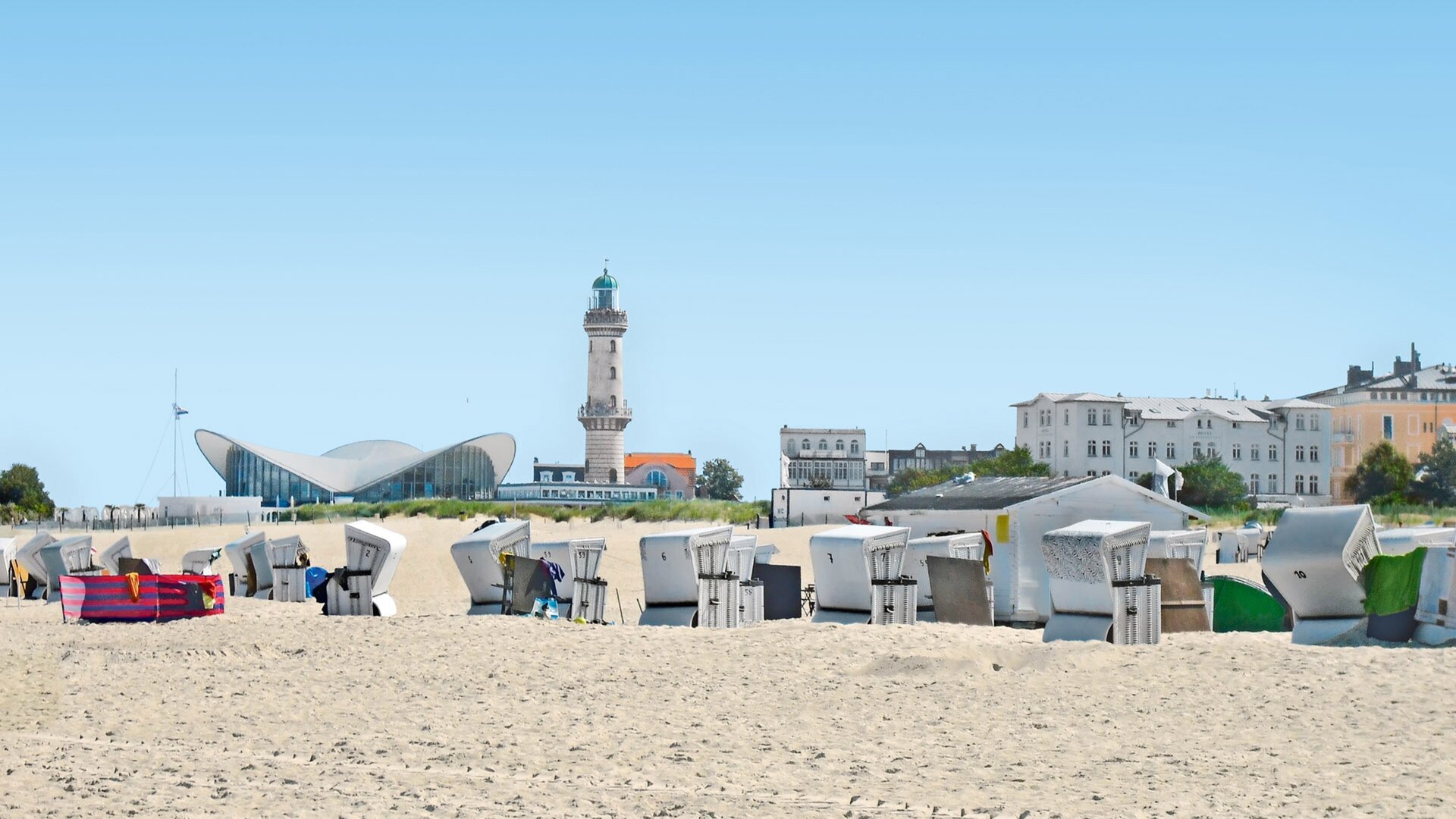 Strandkörbe am Strand von Warnemünde mit Leuchtturm und Teepott.