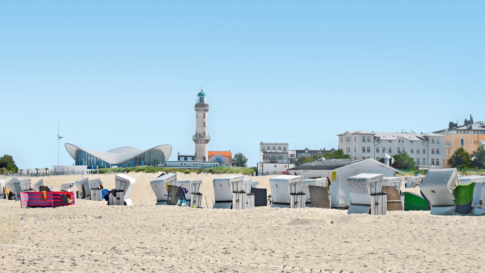 Strandkörbe am Strand von Warnemünde mit Leuchtturm und Teepott.