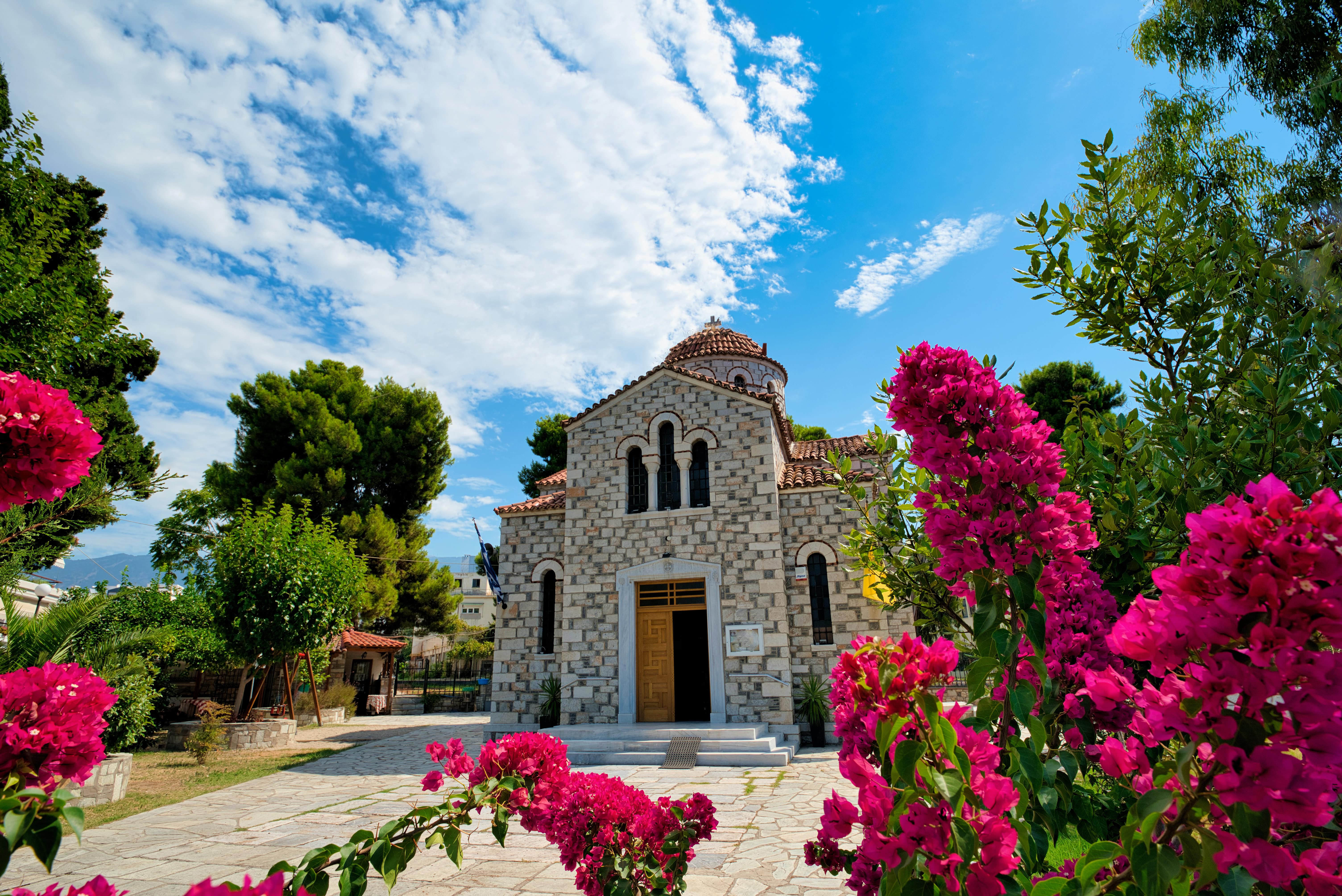 Steinkirche mit rosa Blumen im Vordergrund, blauer Himmel.