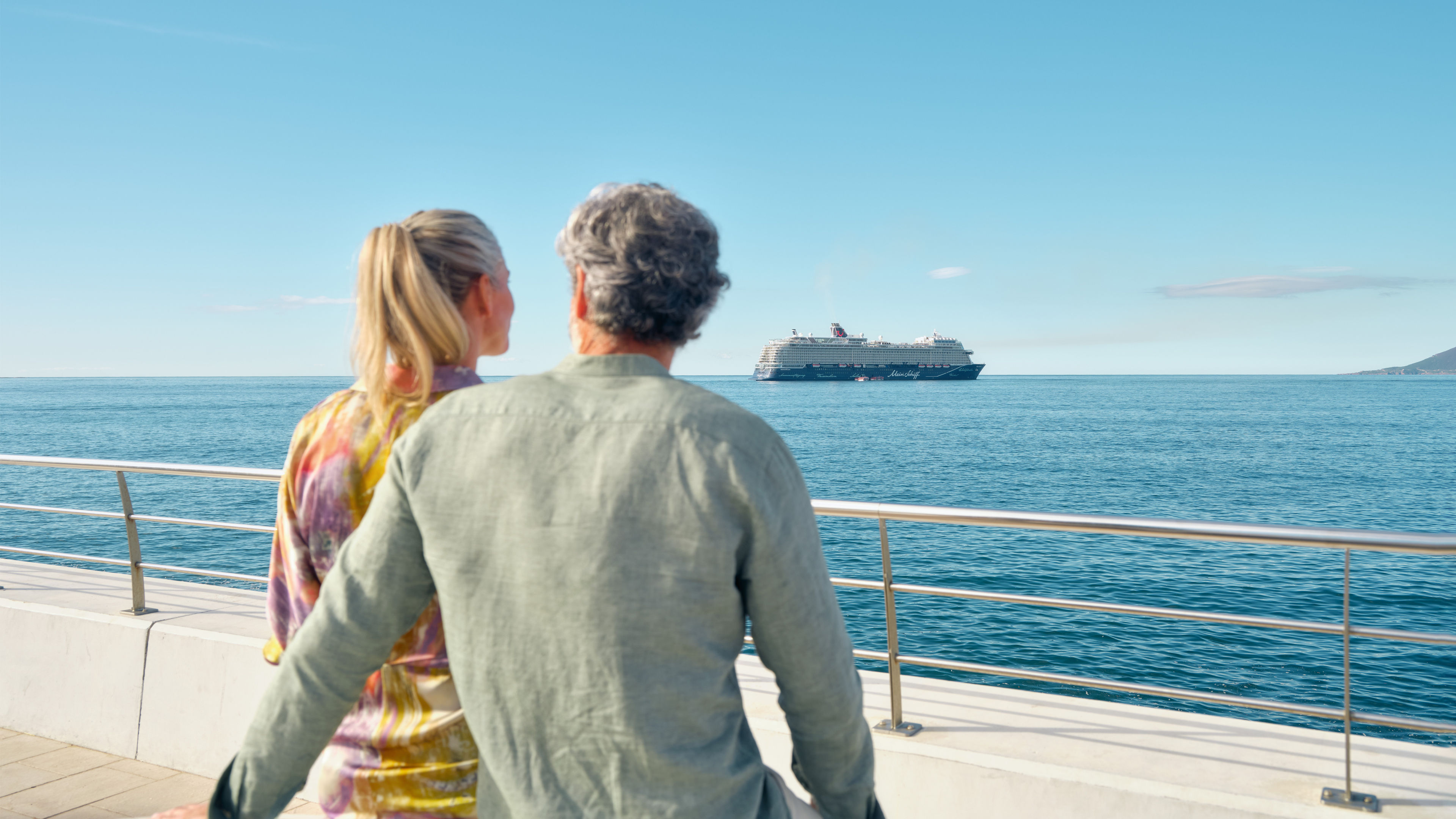 Paar blickt auf Kreuzfahrtschiff der Mein Schiff® Flotte im Meer.