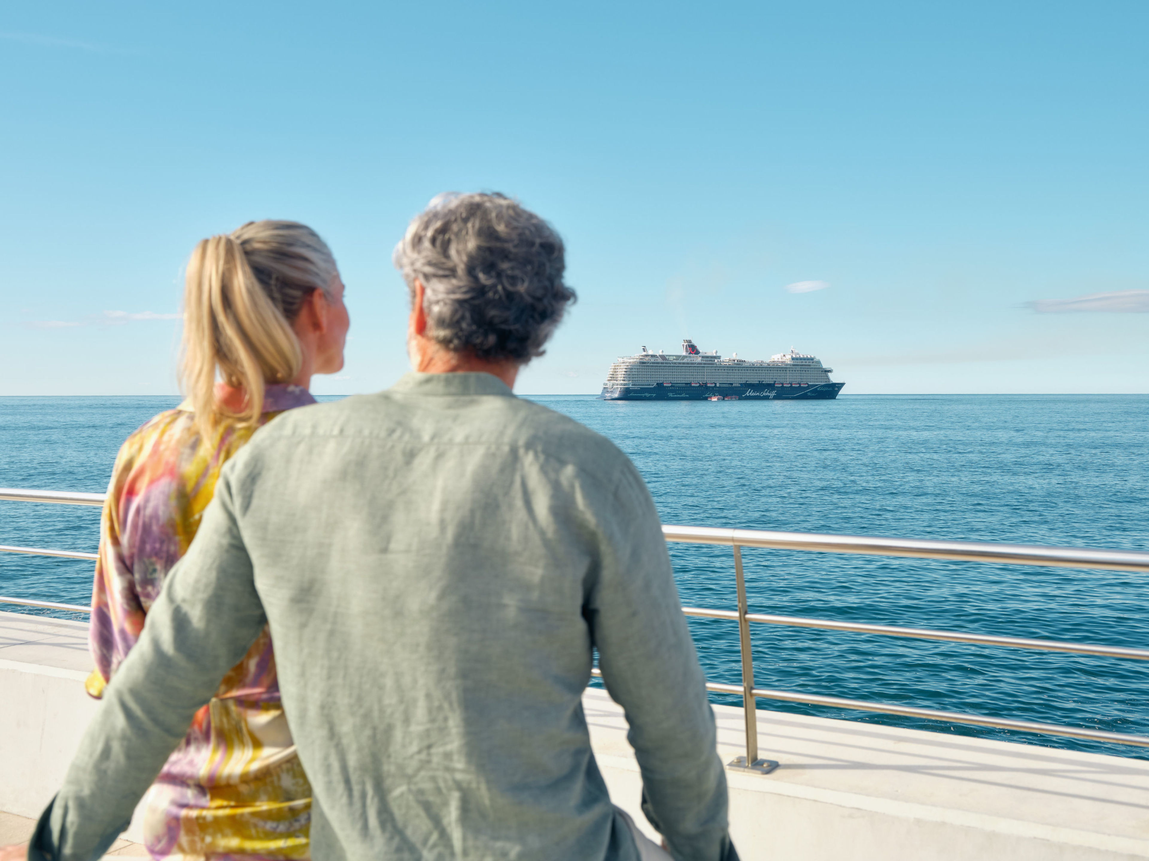 Paar blickt auf Kreuzfahrtschiff der Mein Schiff® Flotte im Meer. Paar blickt auf Kreuzfahrtschiff der Mein Schiff® Flotte im Meer.