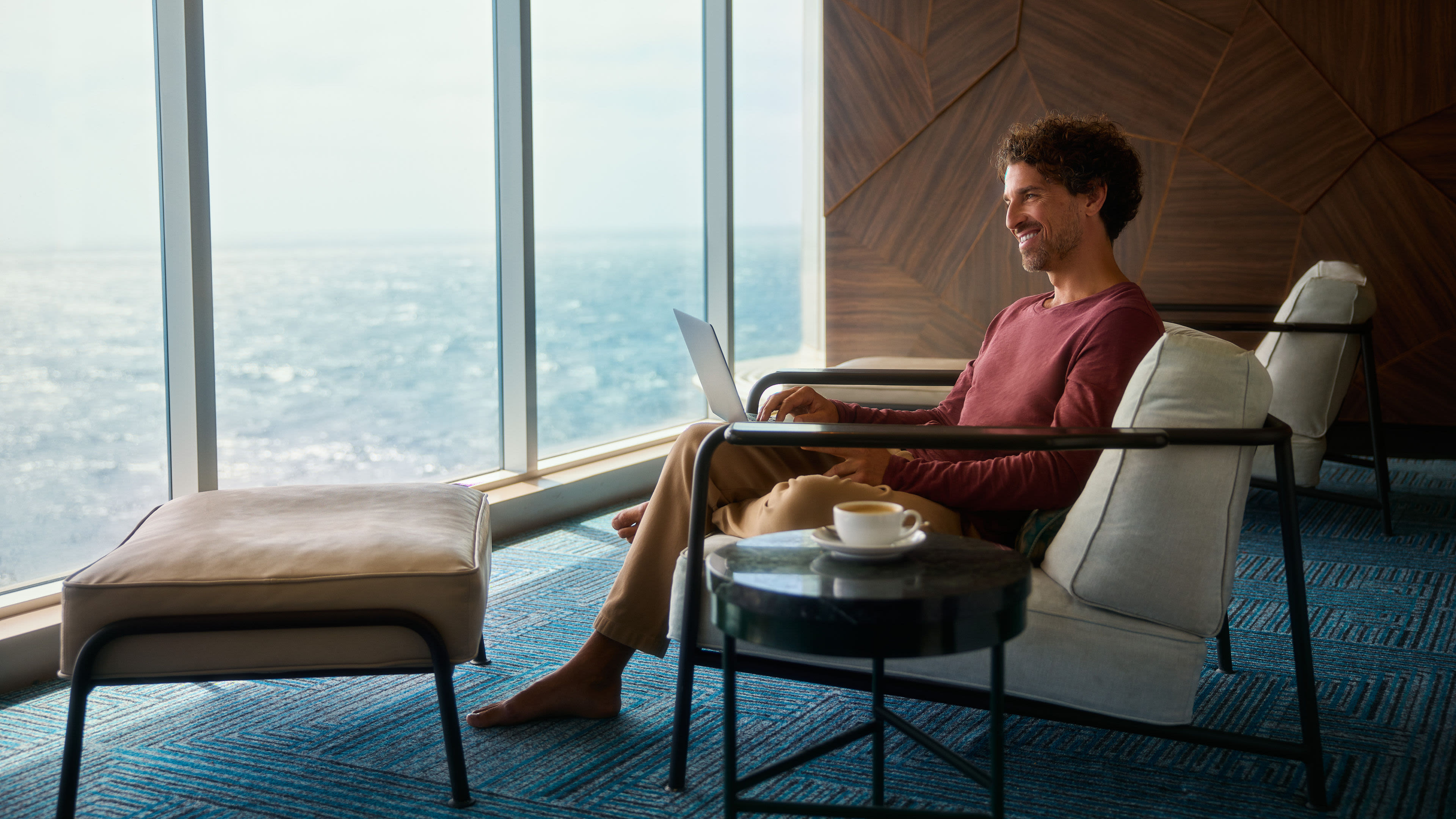 Mann mit Laptop und Kaffee Mann entspannt mit Laptop am Fenster, Meerblick.