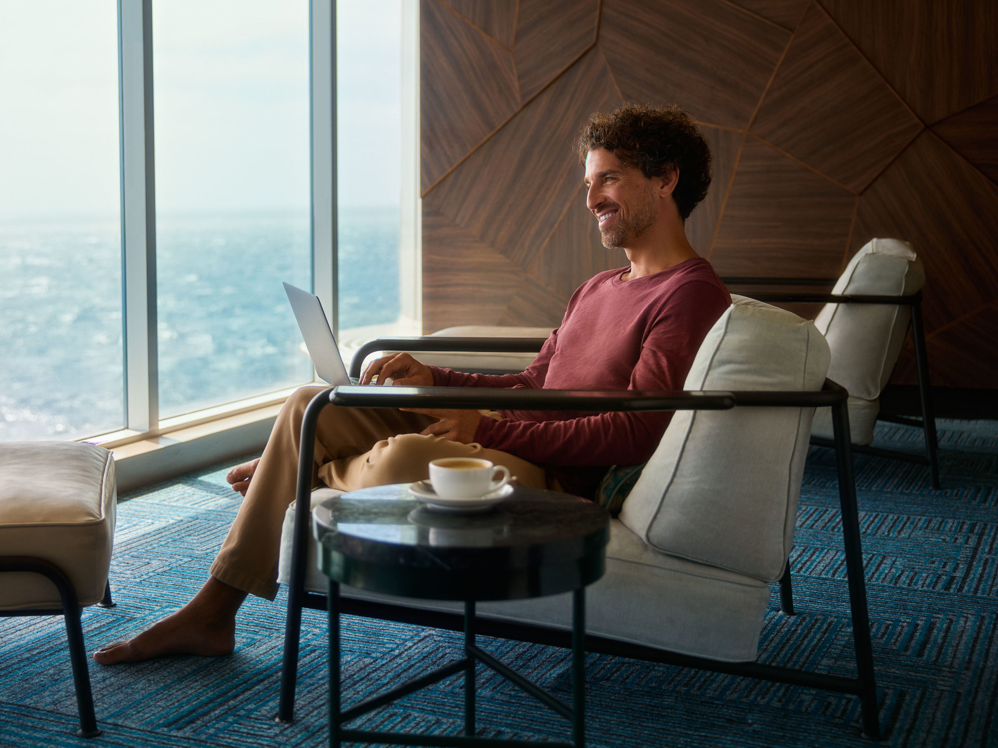 Mann mit Laptop und Kaffee Mann entspannt mit Laptop am Fenster, Meerblick.