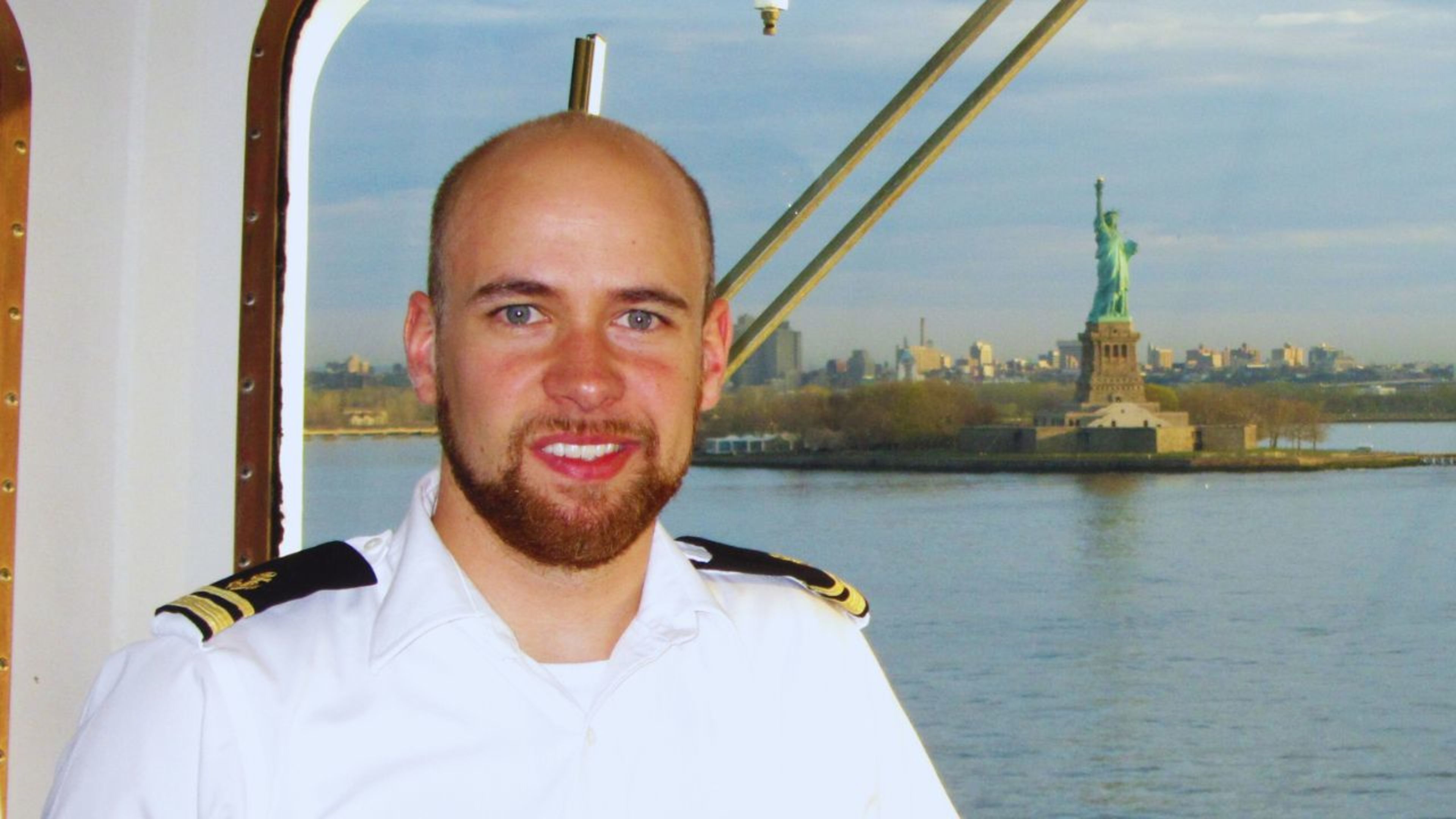 Sven Kassel Mann in Uniform vor Freiheitsstatue, New York Skyline im Hintergrund.