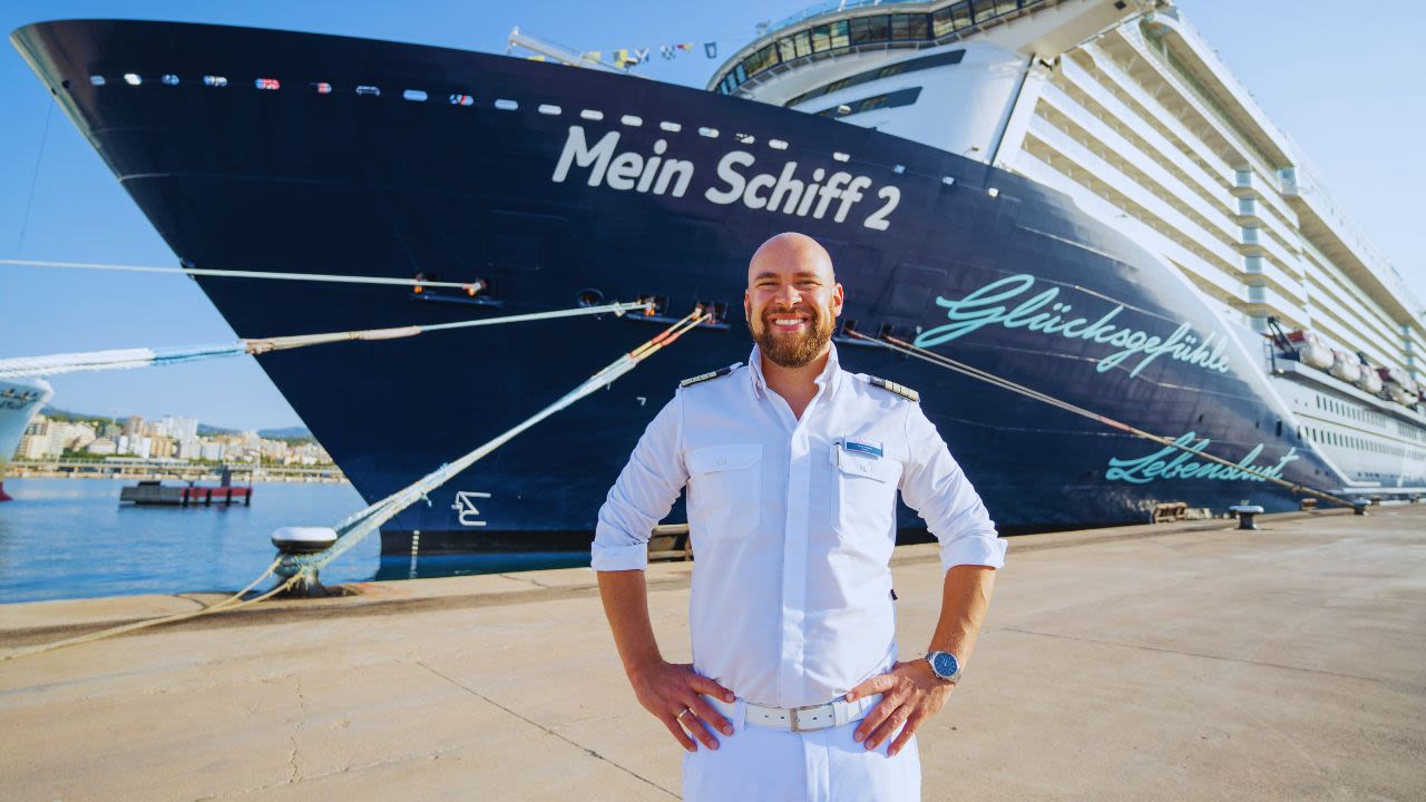 Mann in Uniform vor Kreuzfahrtschiff der Mein Schiff® Flotte im Hafen.