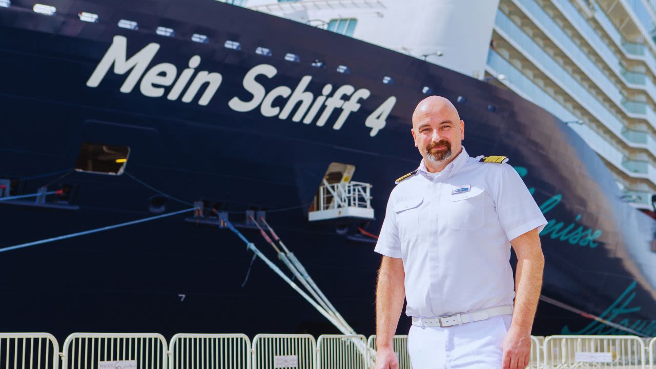 Kapitän in weißer Uniform vor Kreuzfahrtschiff der Mein Schiff® Flotte.
