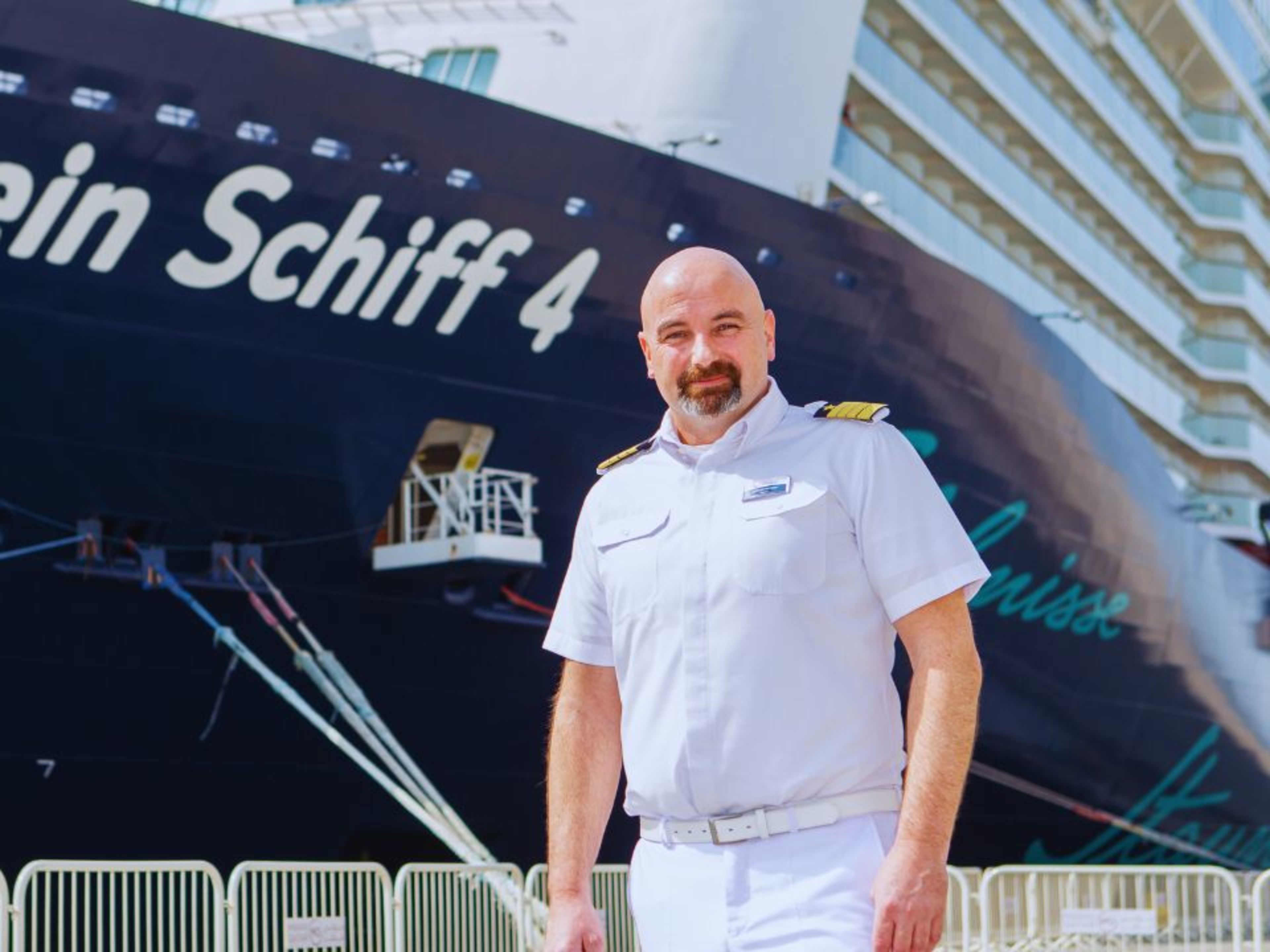 Kapitänsporträt Günter Batzner Kapitän in weißer Uniform vor Kreuzfahrtschiff der Mein Schiff® Flotte.