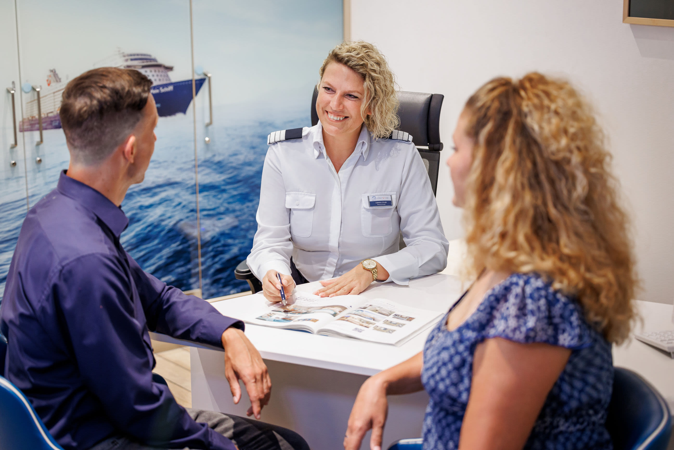 Drei Personen im Beratungsgespräch, Kreuzfahrtschiff der Mein Schiff® Flotte im Hintergrund. Drei Personen im Beratungsgespräch, Kreuzfahrtschiff der Mein Schiff® Flotte im Hintergrund.