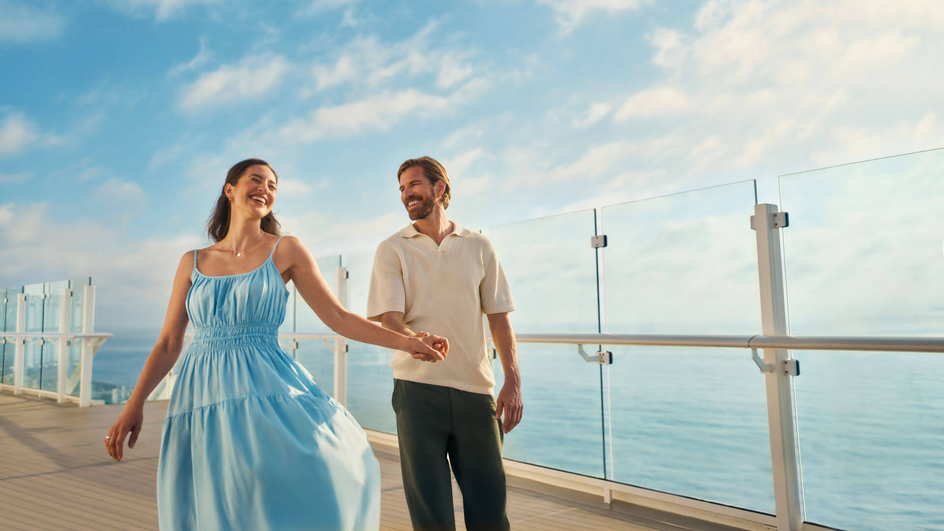 Paar spaziert lachend auf Kreuzfahrtschiffdeck bei sonnigem Wetter.
