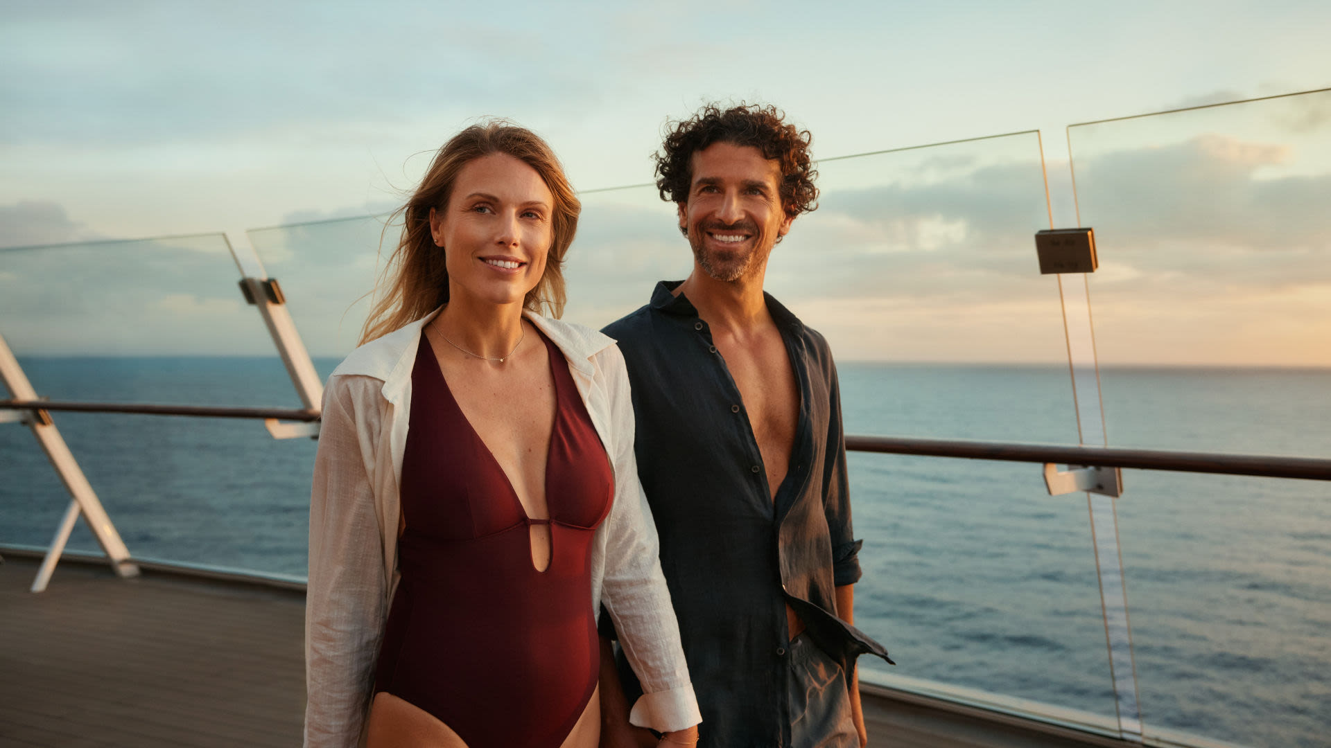 Paar auf Kreuzfahrtschiff bei Sonnenuntergang, lächelnd, Meer im Hintergrund.