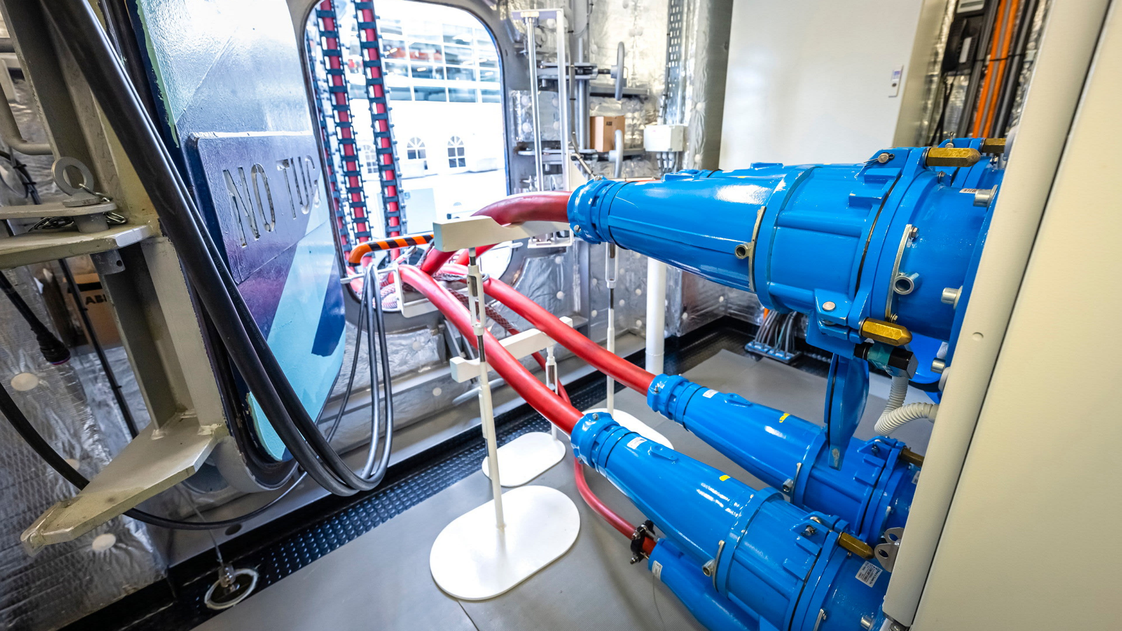 Blaue Kabel und rote Rohre in einem technischen Raum.