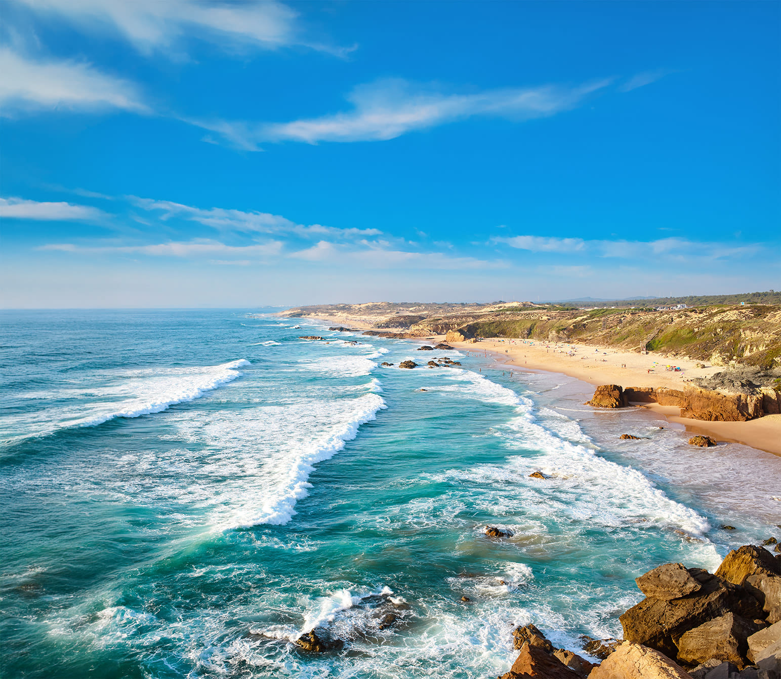 Küste mit Wellen, blauem Himmel und Sandstrand in Portugal.