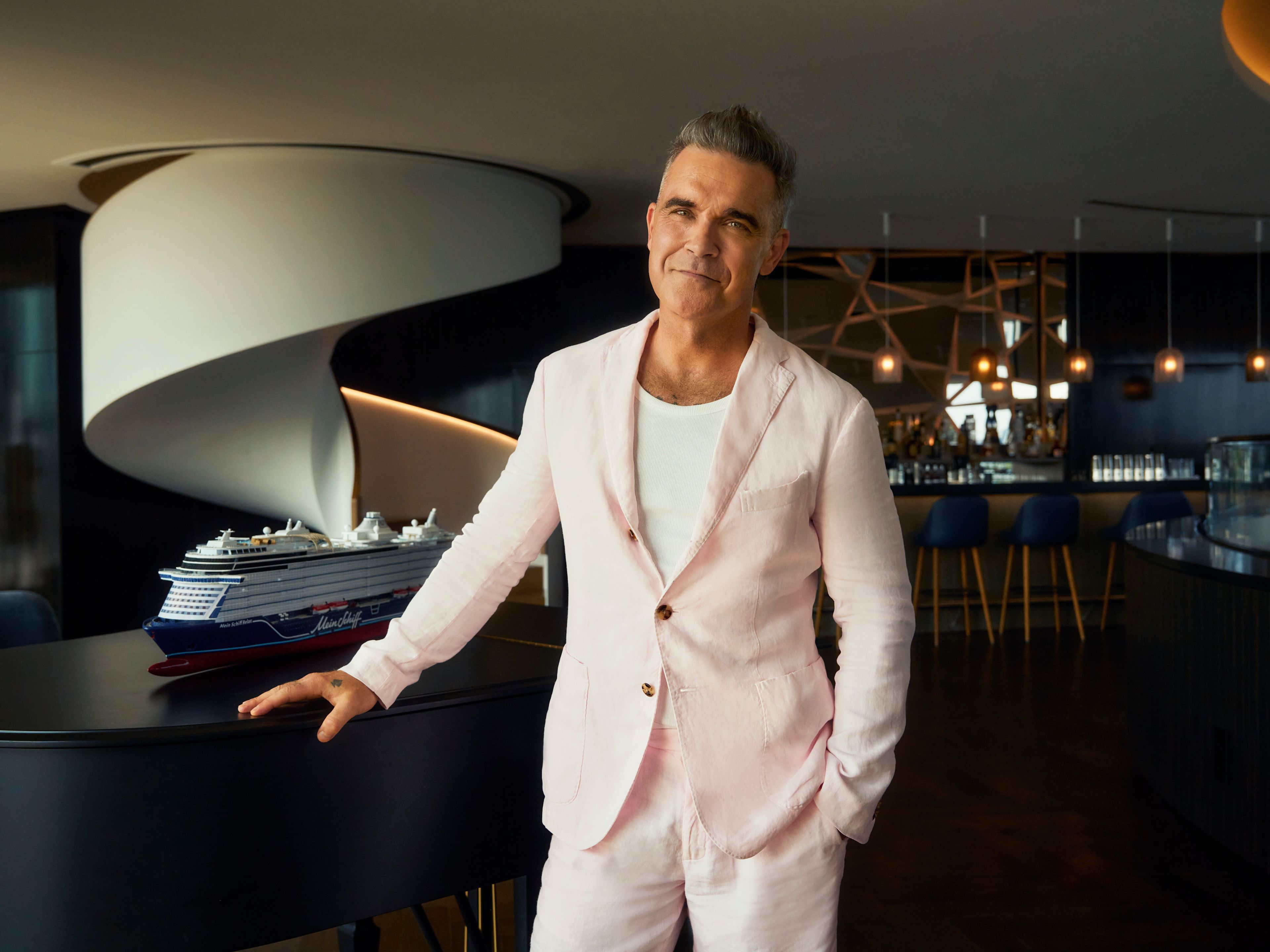 Mann in rosa Anzug neben Modell eines Kreuzfahrtschiffs. Mann in rosa Anzug neben Modell eines Kreuzfahrtschiffs.