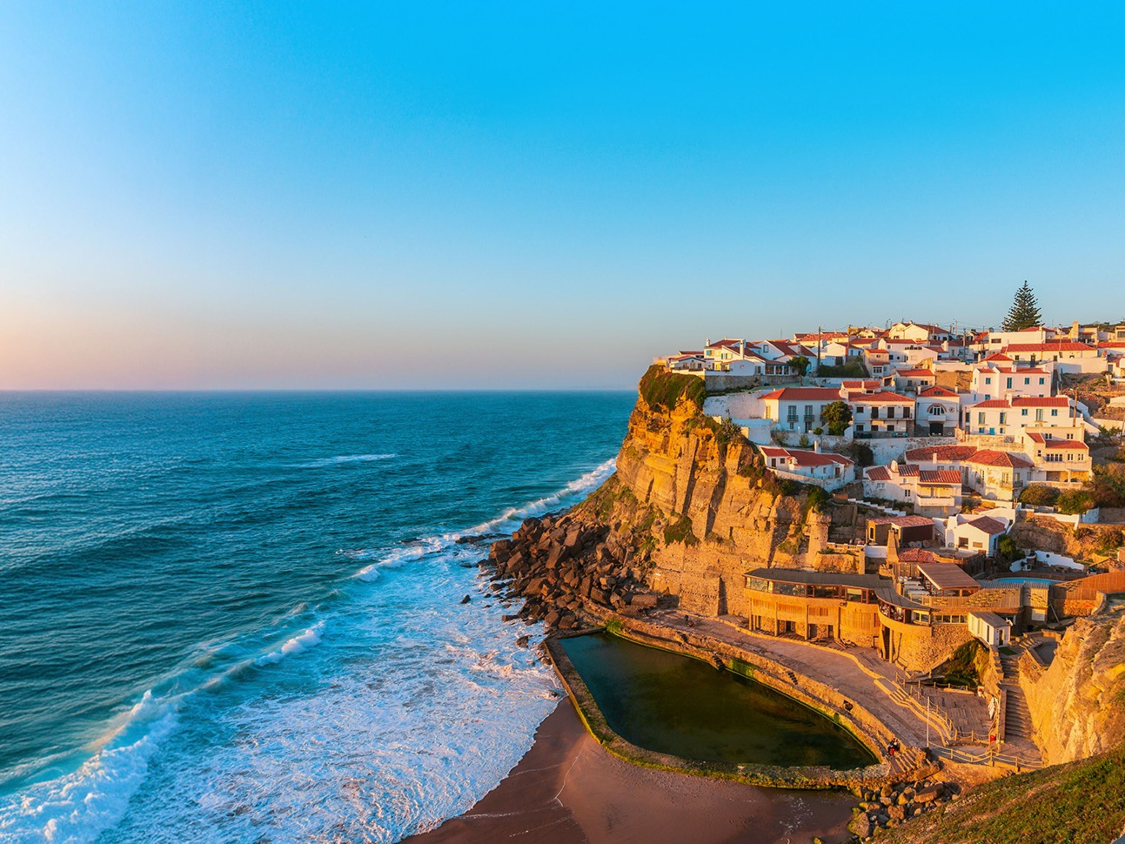 Atlantikküste Portugal Küstenstadt auf Klippe bei Sonnenuntergang, blaues Meer, bunte Häuser.
