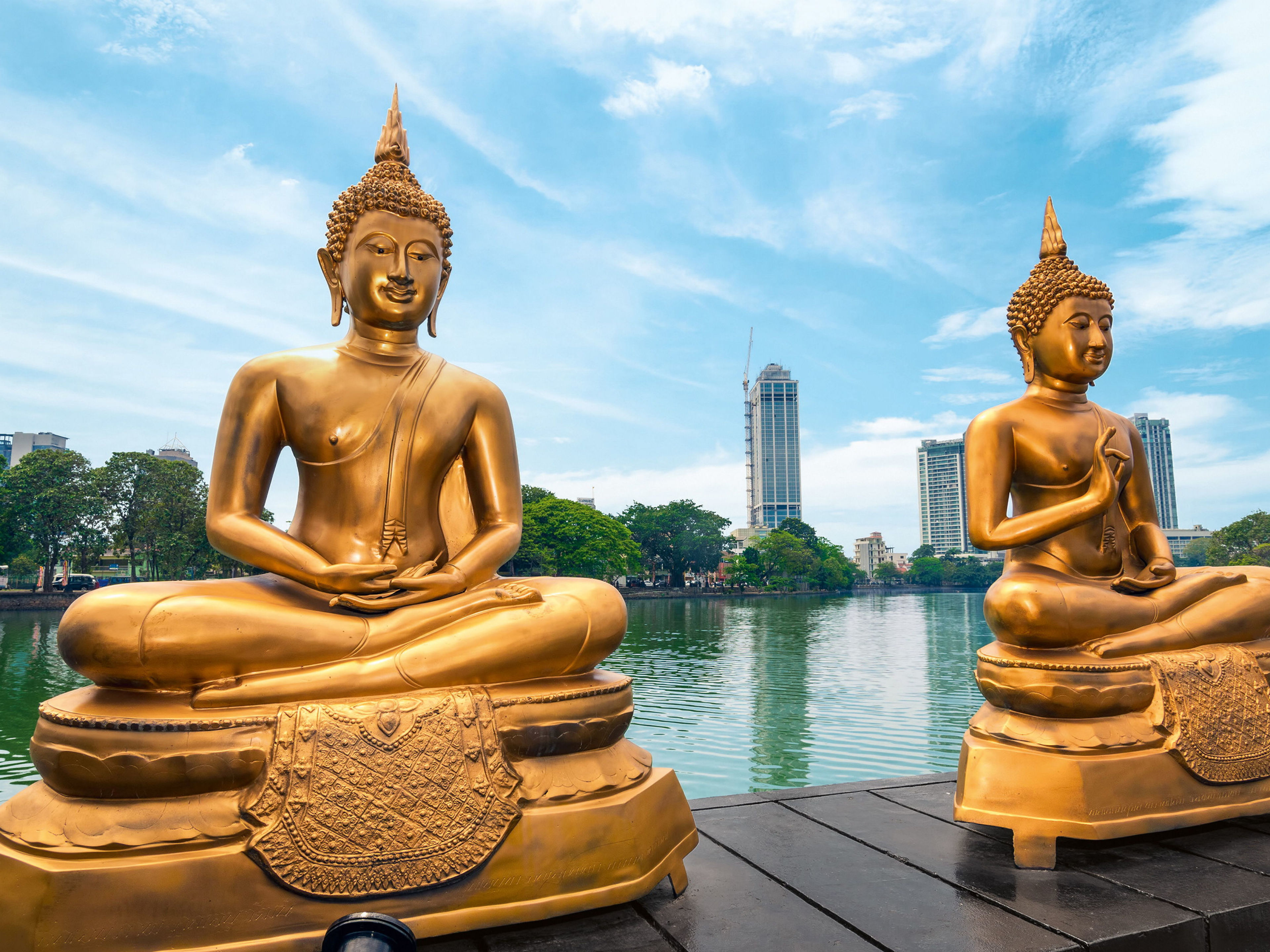 Goldene Buddha-Statuen am Wasser, Stadt im Hintergrund, blauer Himmel. Goldene Buddha-Statuen am Wasser, Stadt im Hintergrund, blauer Himmel.