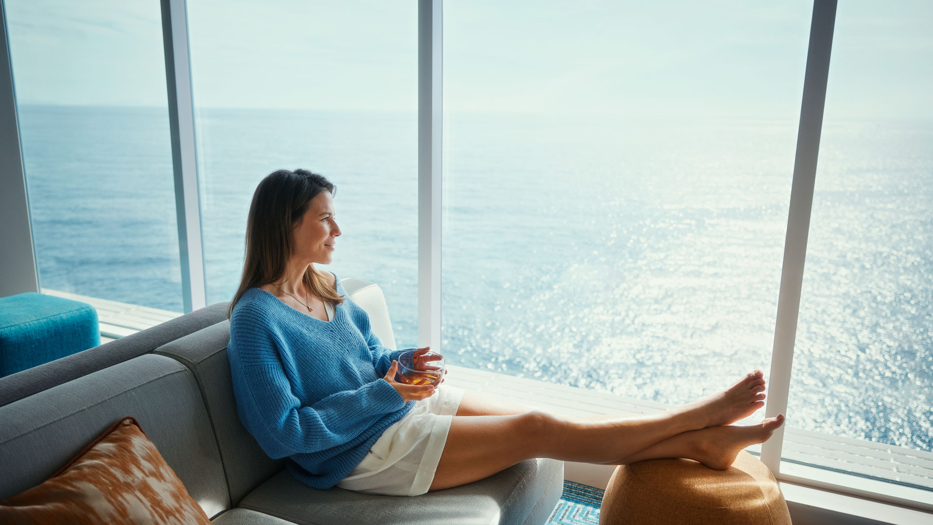 Frau in blauem Pullover entspannt auf Sofa, Meerblick.