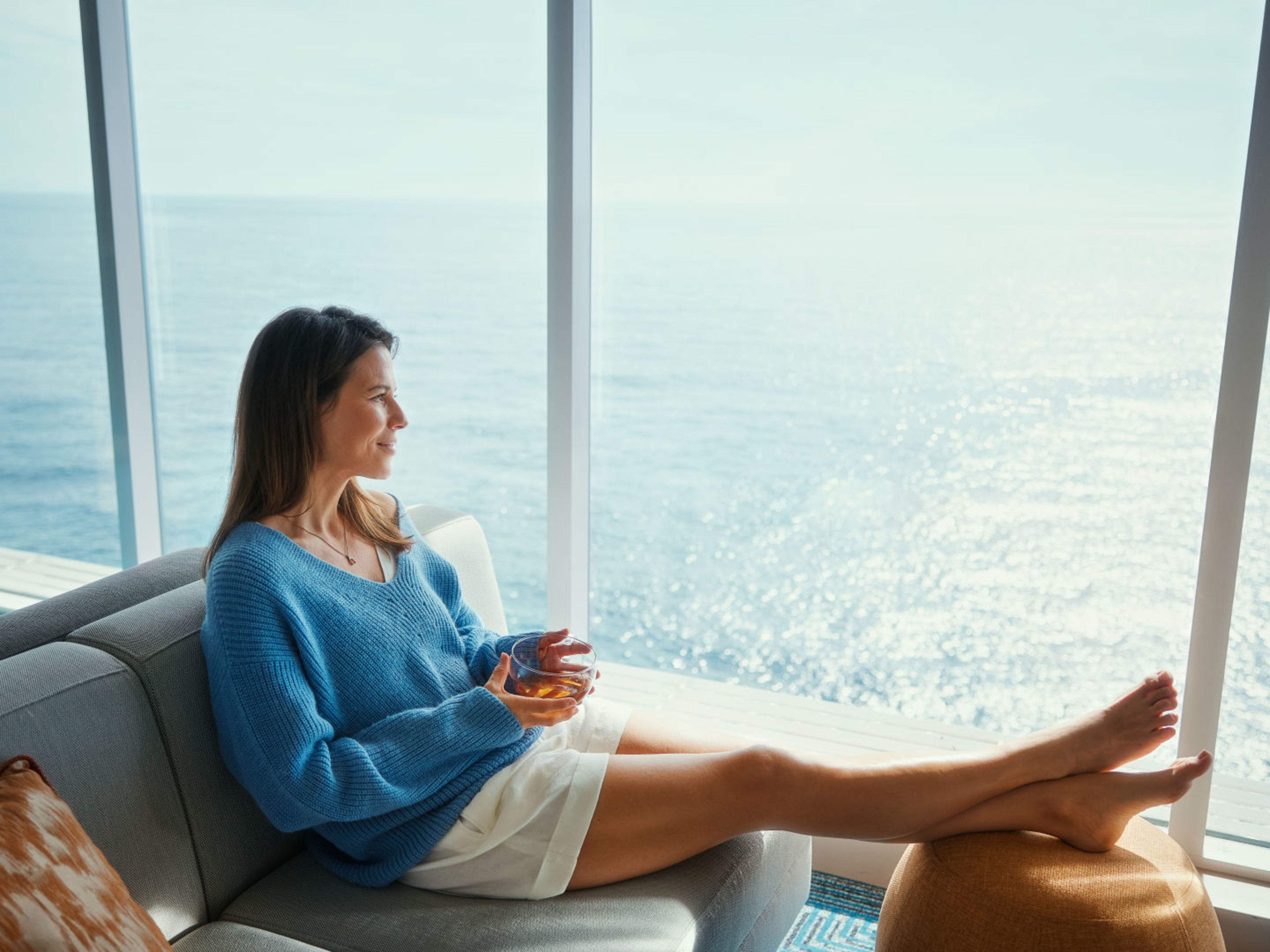 Frau in blauem Pullover entspannt auf Sofa, Meerblick. Frau in blauem Pullover entspannt auf Sofa, Meerblick.