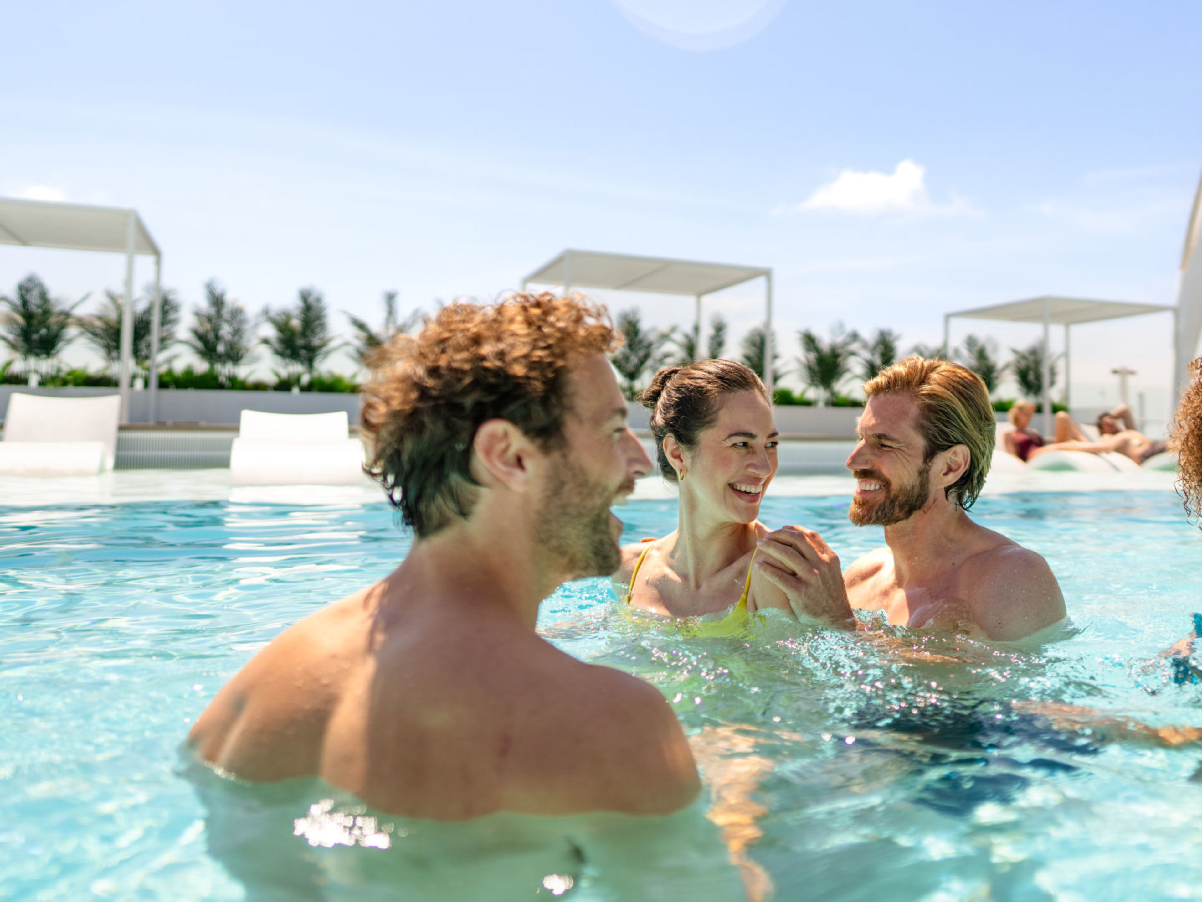 Zwei Paare unterhalten sich im Pool Vier lachende Menschen im Pool bei Sonnenschein.