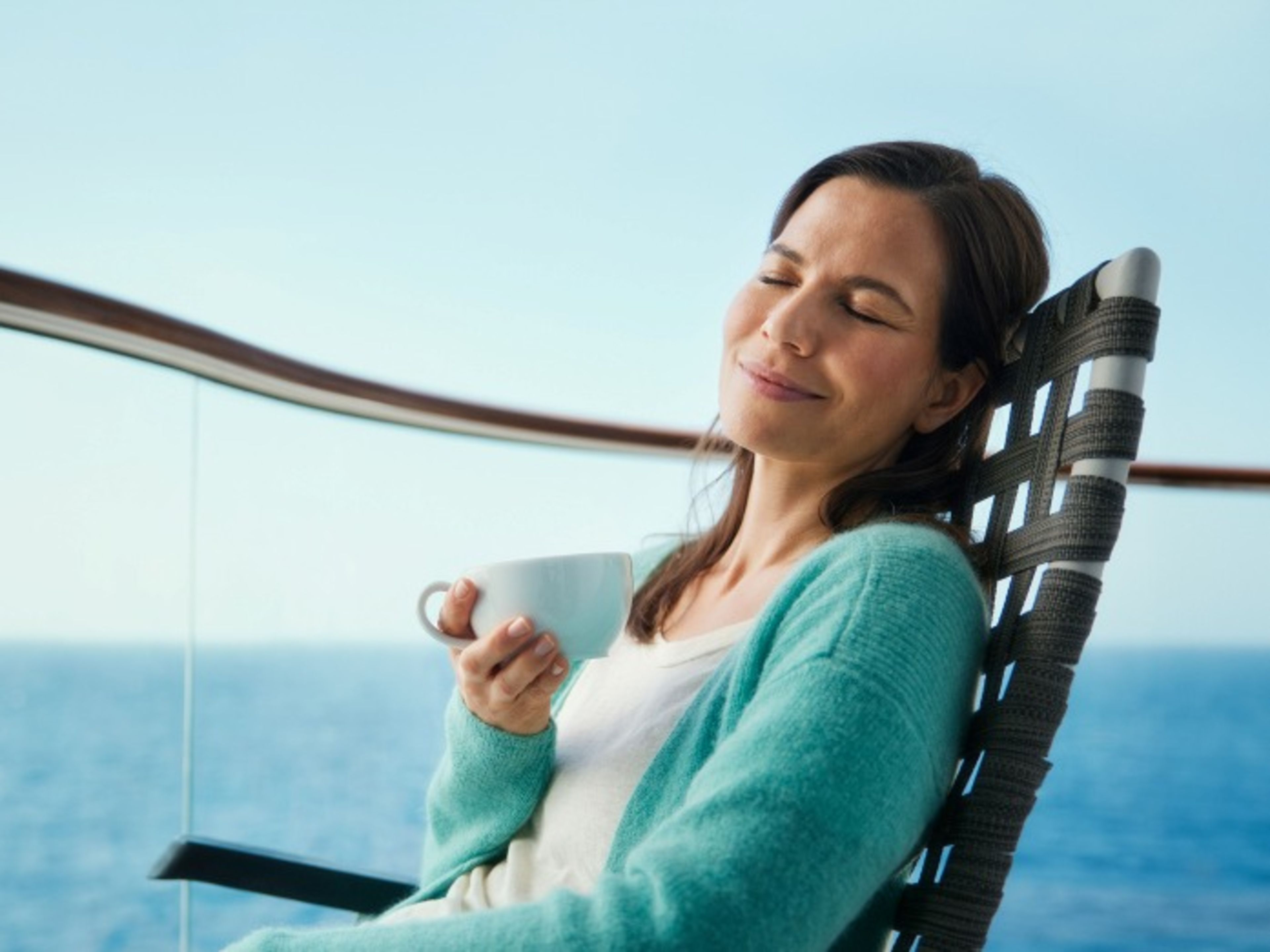 Frau genießt Kaffee auf dem Balkon der Kabine Frau entspannt mit Tasse auf Kreuzfahrtschiff, Meerblick.