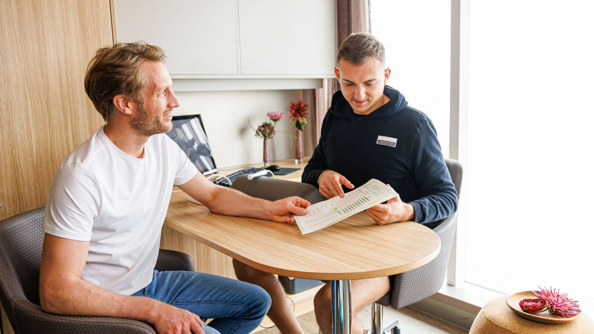 Zwei Männer am Tisch, besprechen Dokument, helle Umgebung.