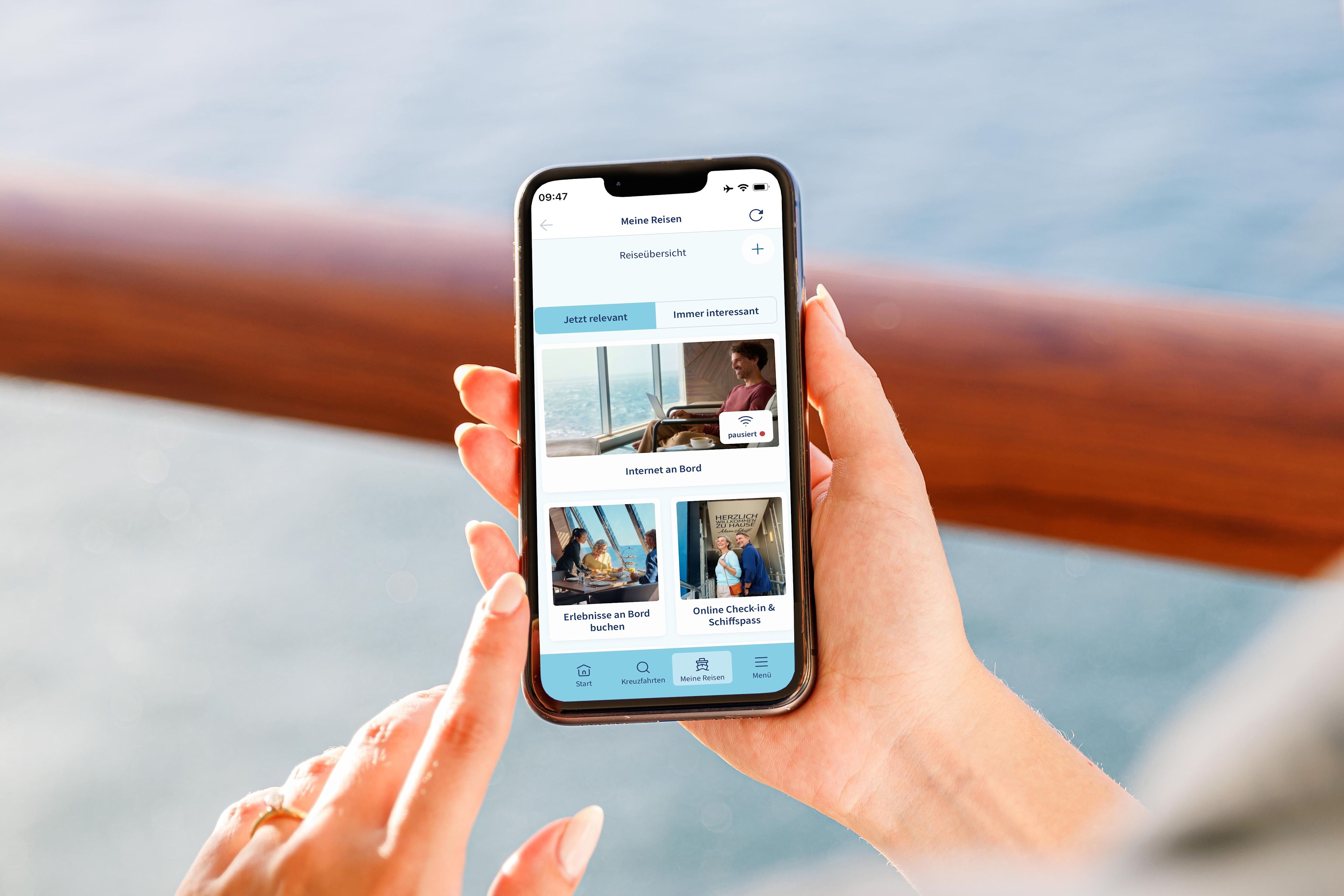 Person hält Smartphone mit Kreuzfahrt-App, Meer im Hintergrund.