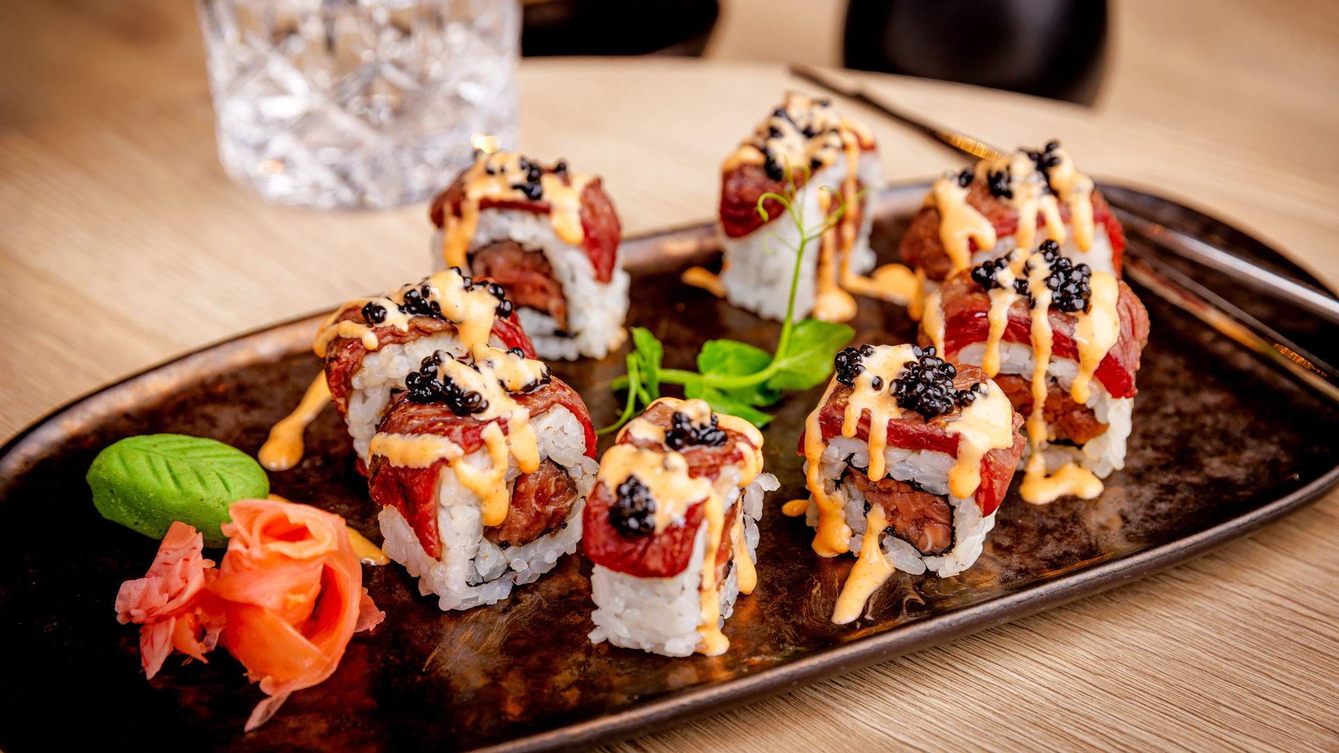 Sushi-Rollen mit Lachs, Kaviar und Sauce auf schwarzem Teller.