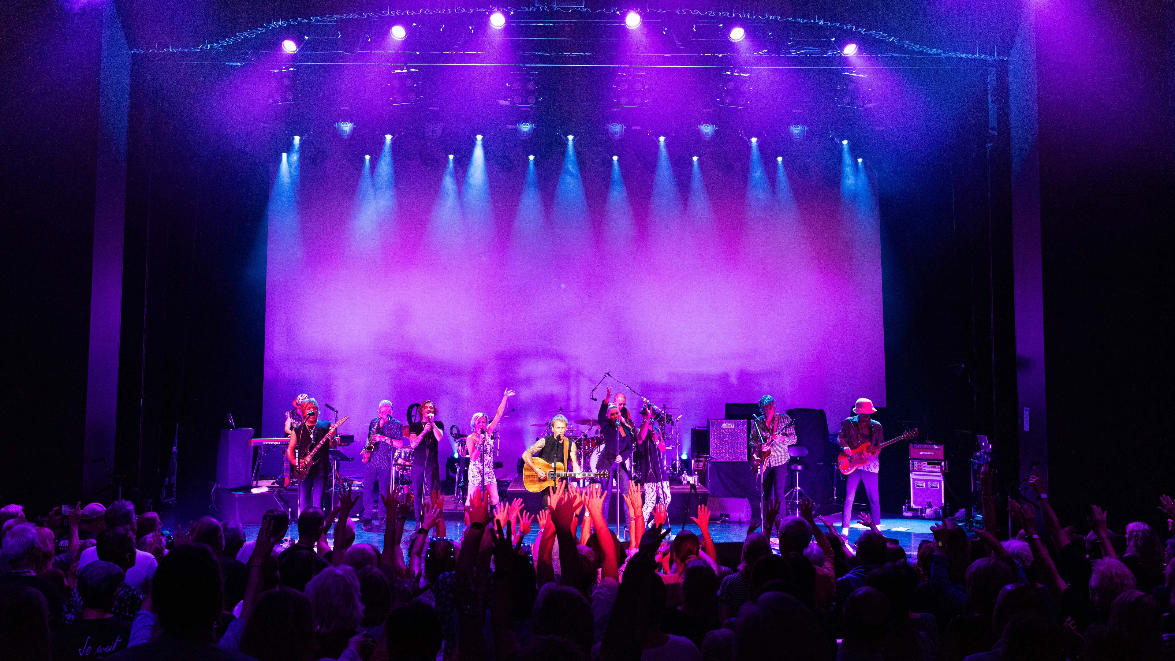 Band spielt auf Bühne mit lila Beleuchtung, jubelndes Publikum. Band spielt auf Bühne mit lila Beleuchtung, jubelndes Publikum.