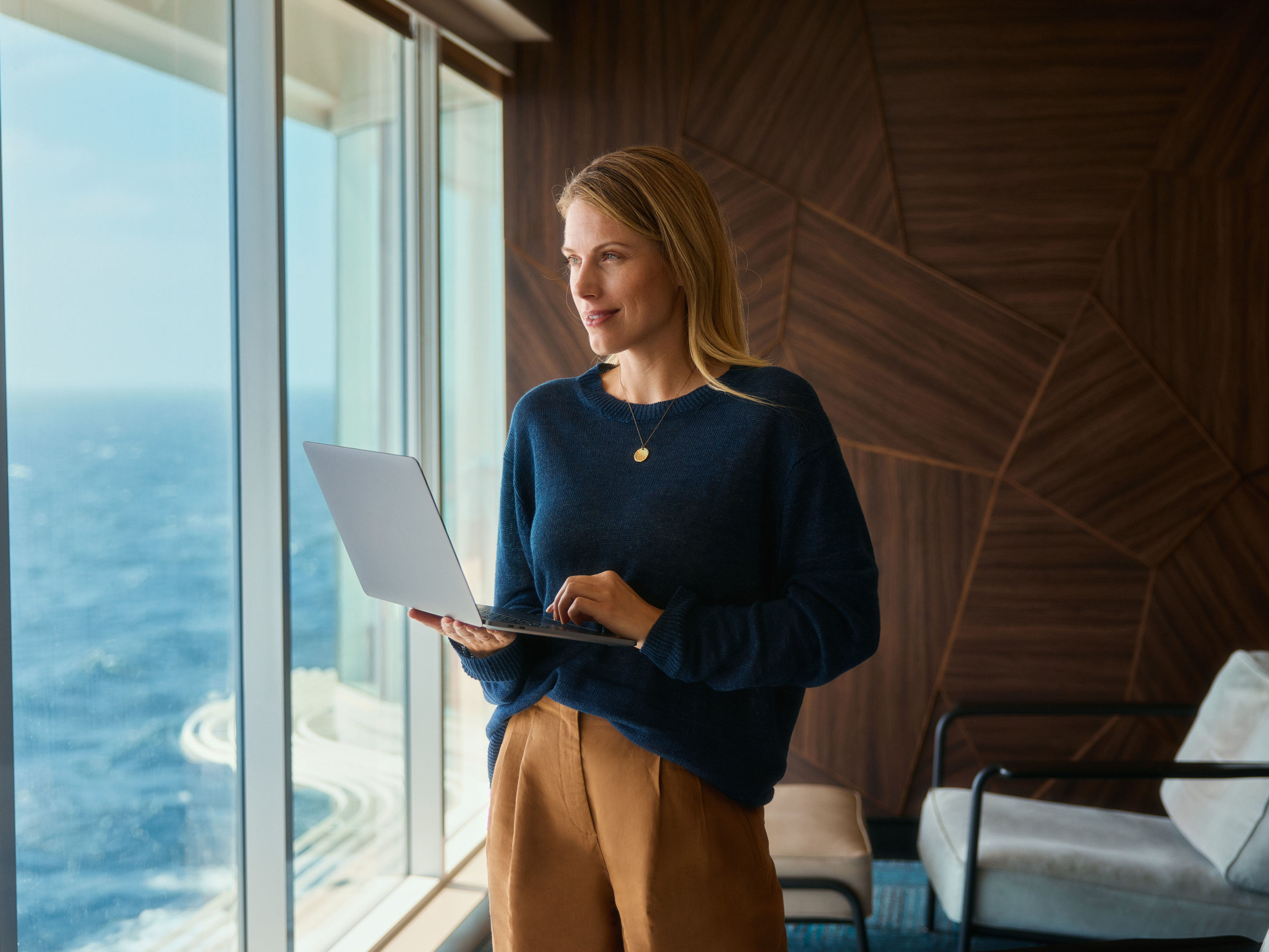 Frau mit Laptop, blickt aus Fenster auf Meer. Frau mit Laptop, blickt aus Fenster auf Meer.