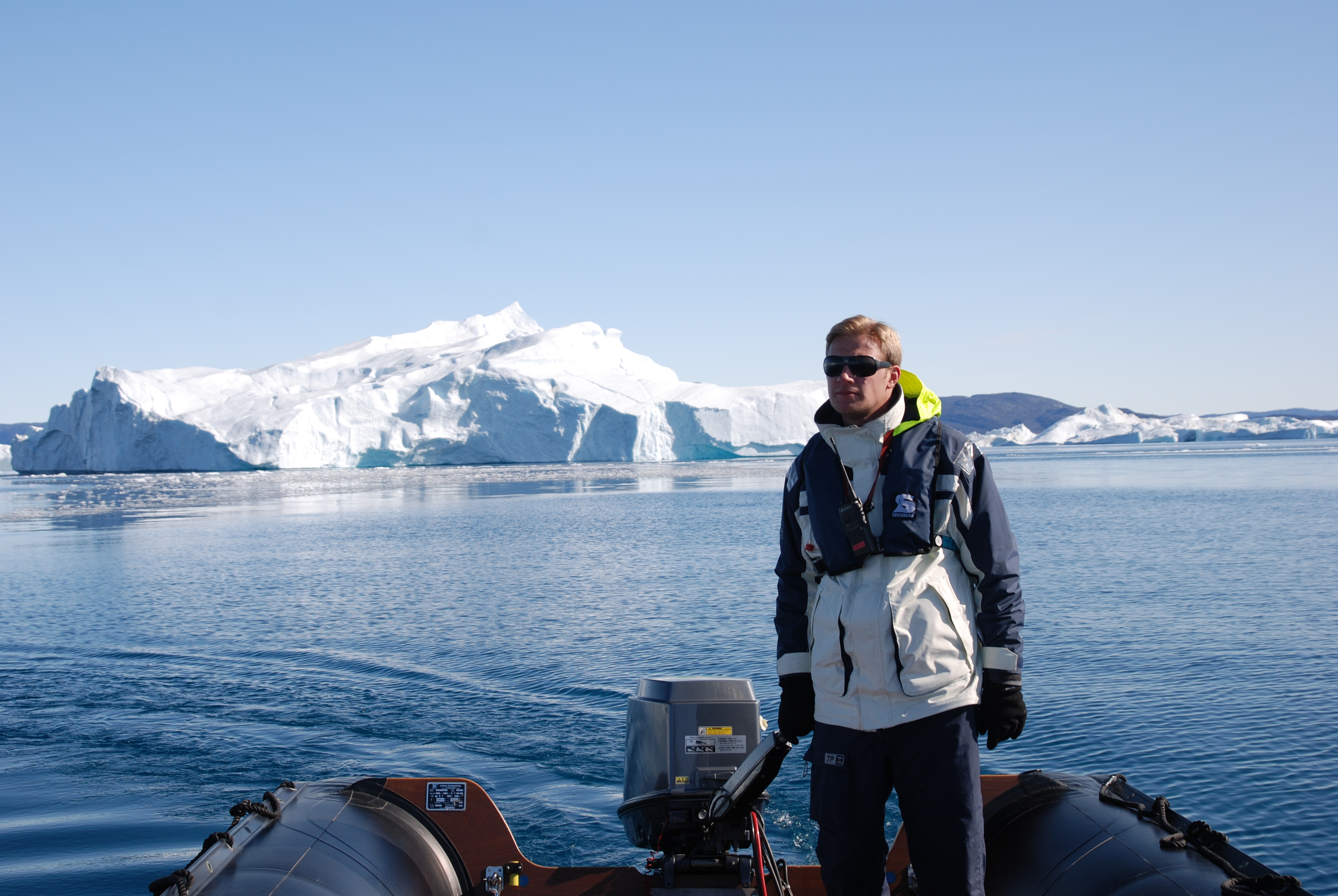 Mann auf Boot vor Eisberg in arktischer Landschaft.