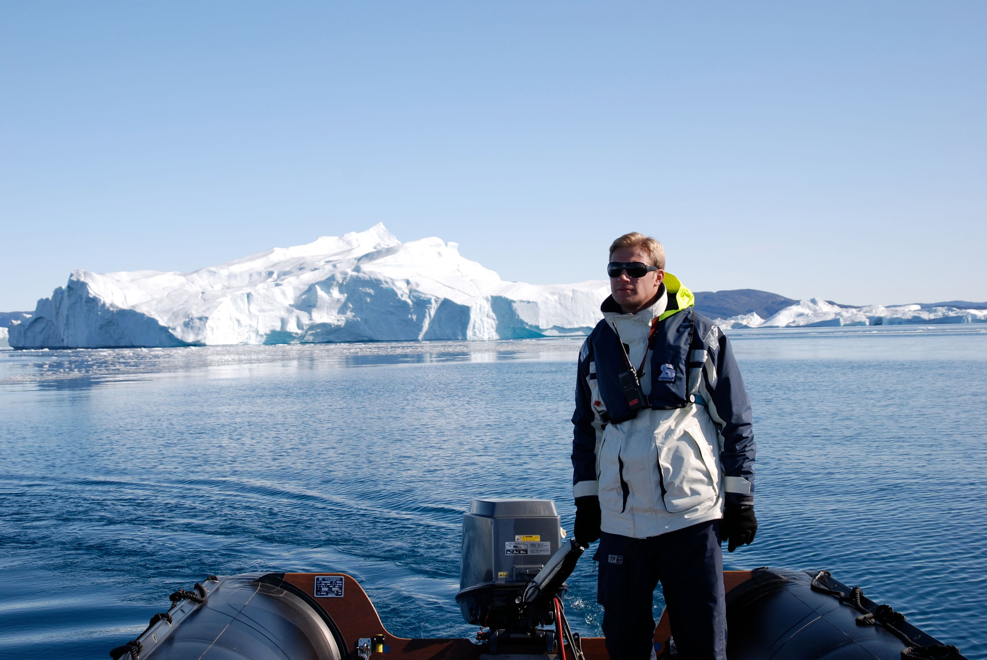 Mann auf Boot vor Eisberg in arktischer Landschaft.