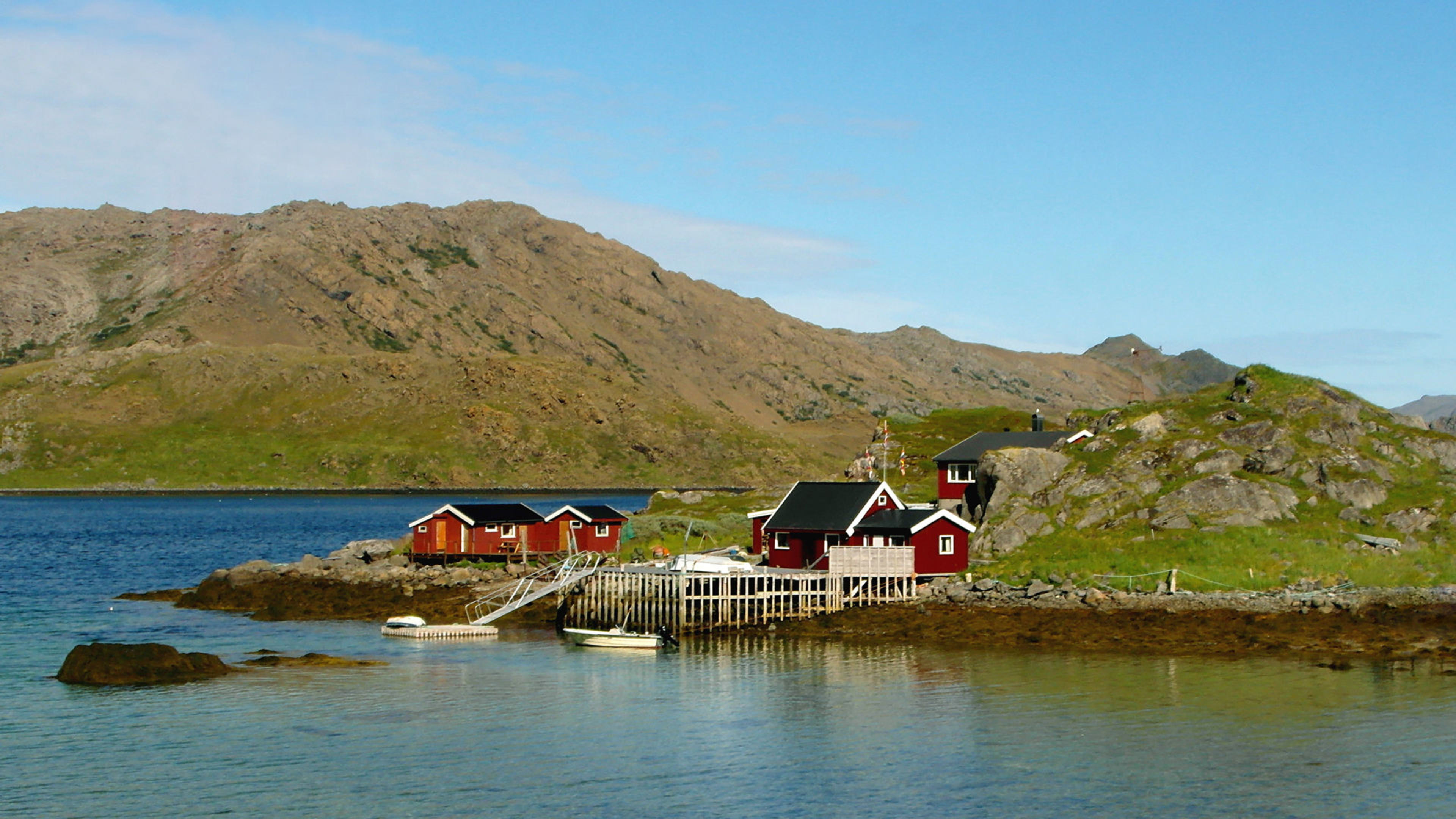 Rote Hütten am Fjord, umgeben von Bergen und blauem Himmel. Rote Hütten am Fjord, umgeben von Bergen und blauem Himmel.