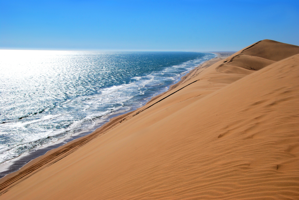Sanddünen treffen auf das Meer unter blauem Himmel.